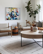 Modern living room with a round wooden coffee table, chairs, and a colorful abstract painting on the wall.
