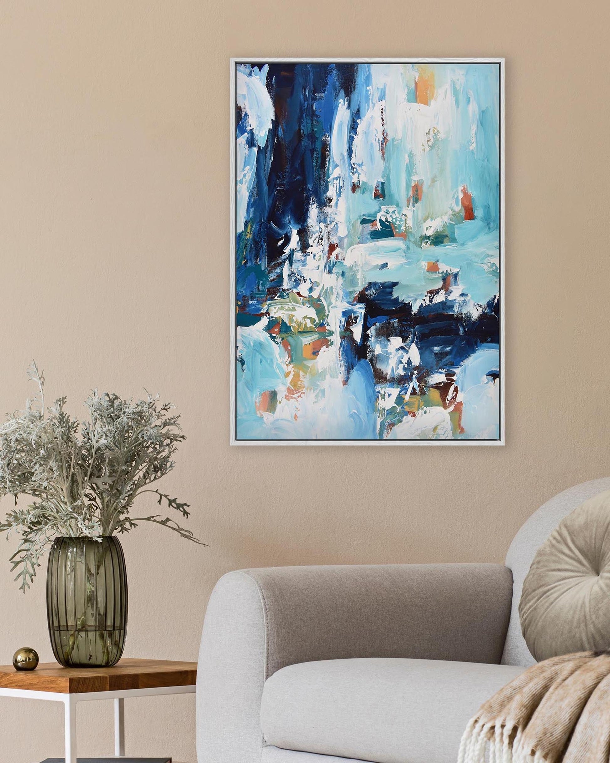 Abstract painting on a beige wall above a sofa with a vase and plant.