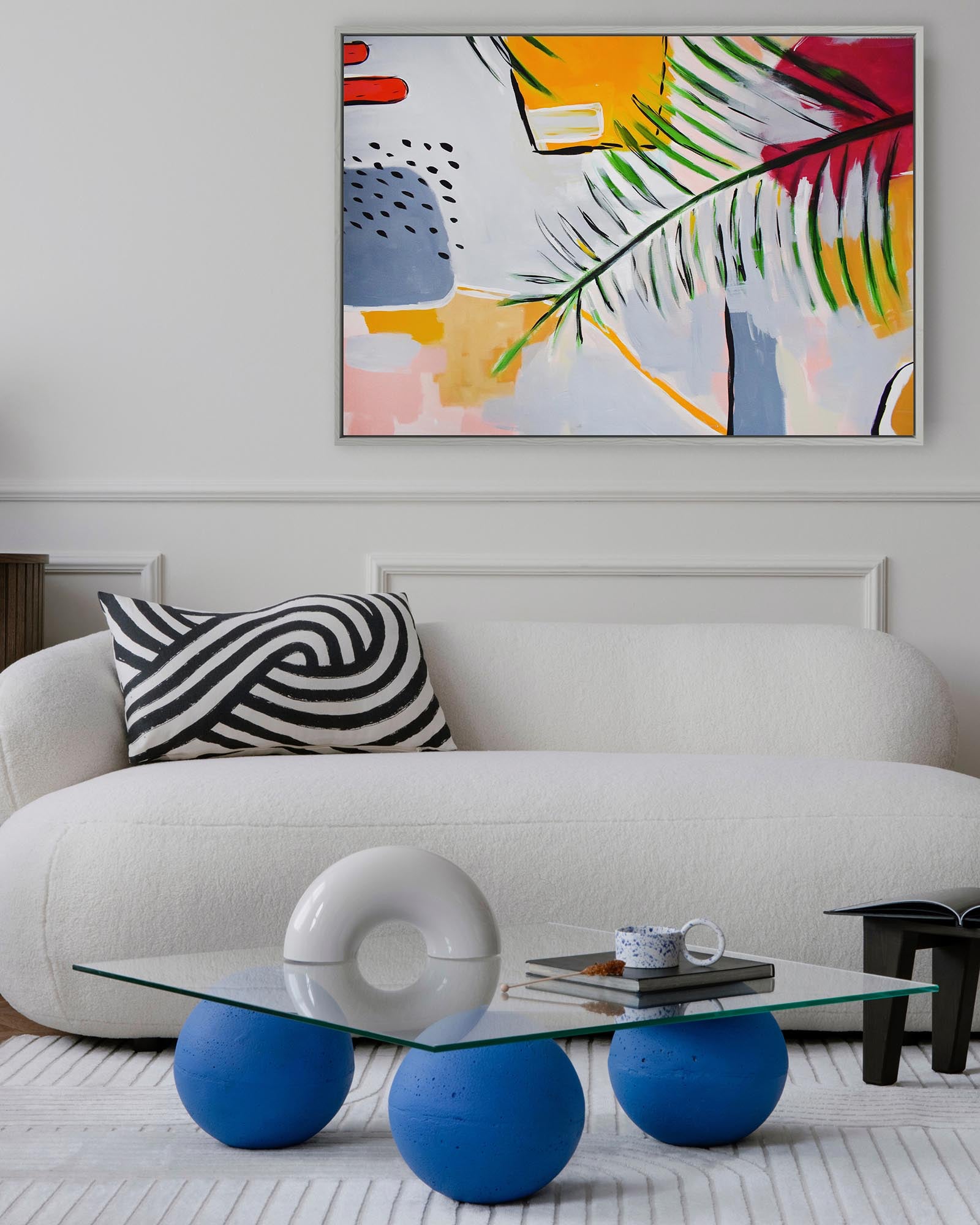Modern living room with a white sofa, abstract art, and a glass coffee table with blue spherical bases.