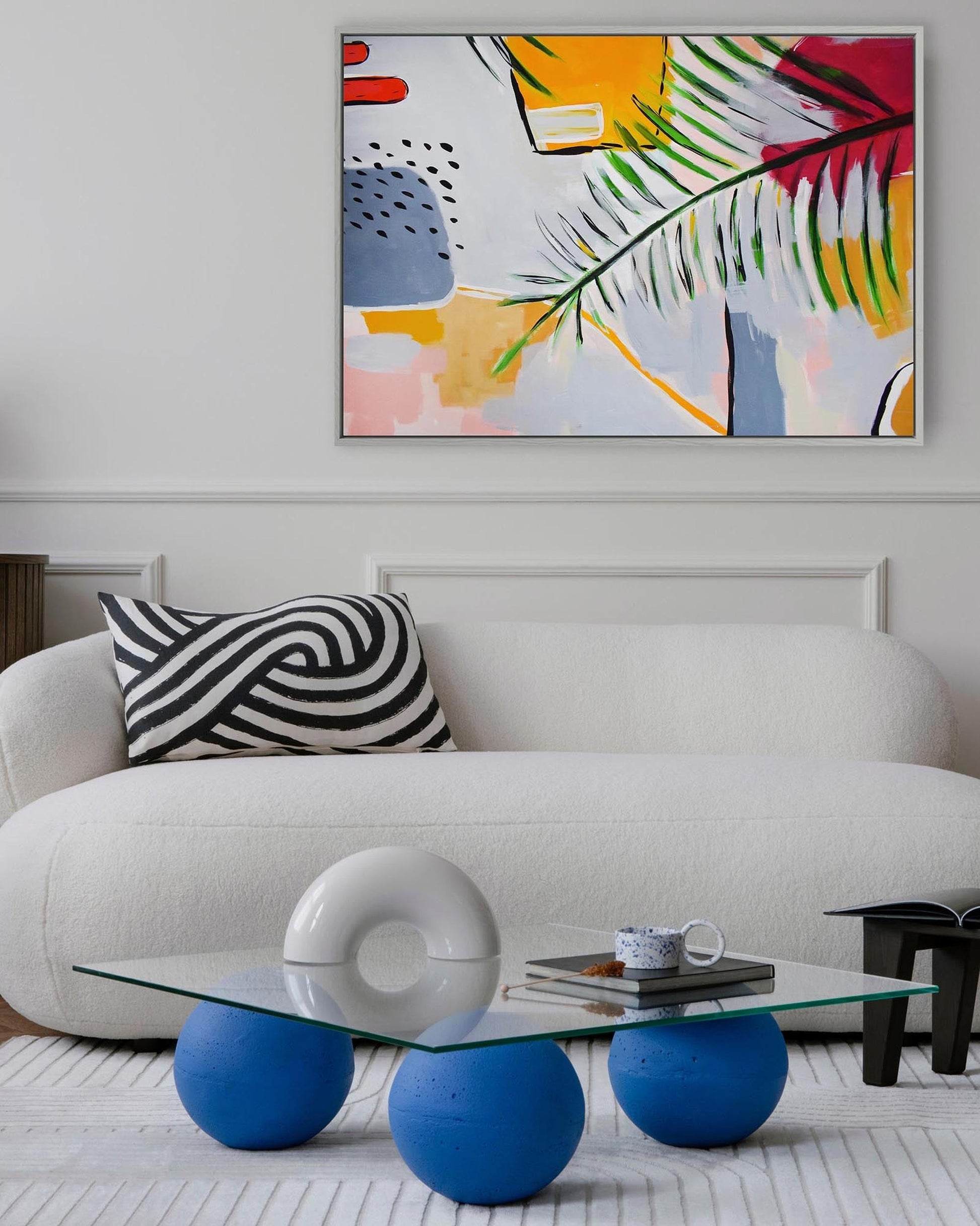 Modern living room with a white sofa, abstract art, and a glass coffee table with blue spherical bases.