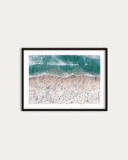 Framed artwork of a beach scene with waves on a white wall