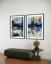 Two abstract art pieces on a wall above a green ottoman and wooden side table.