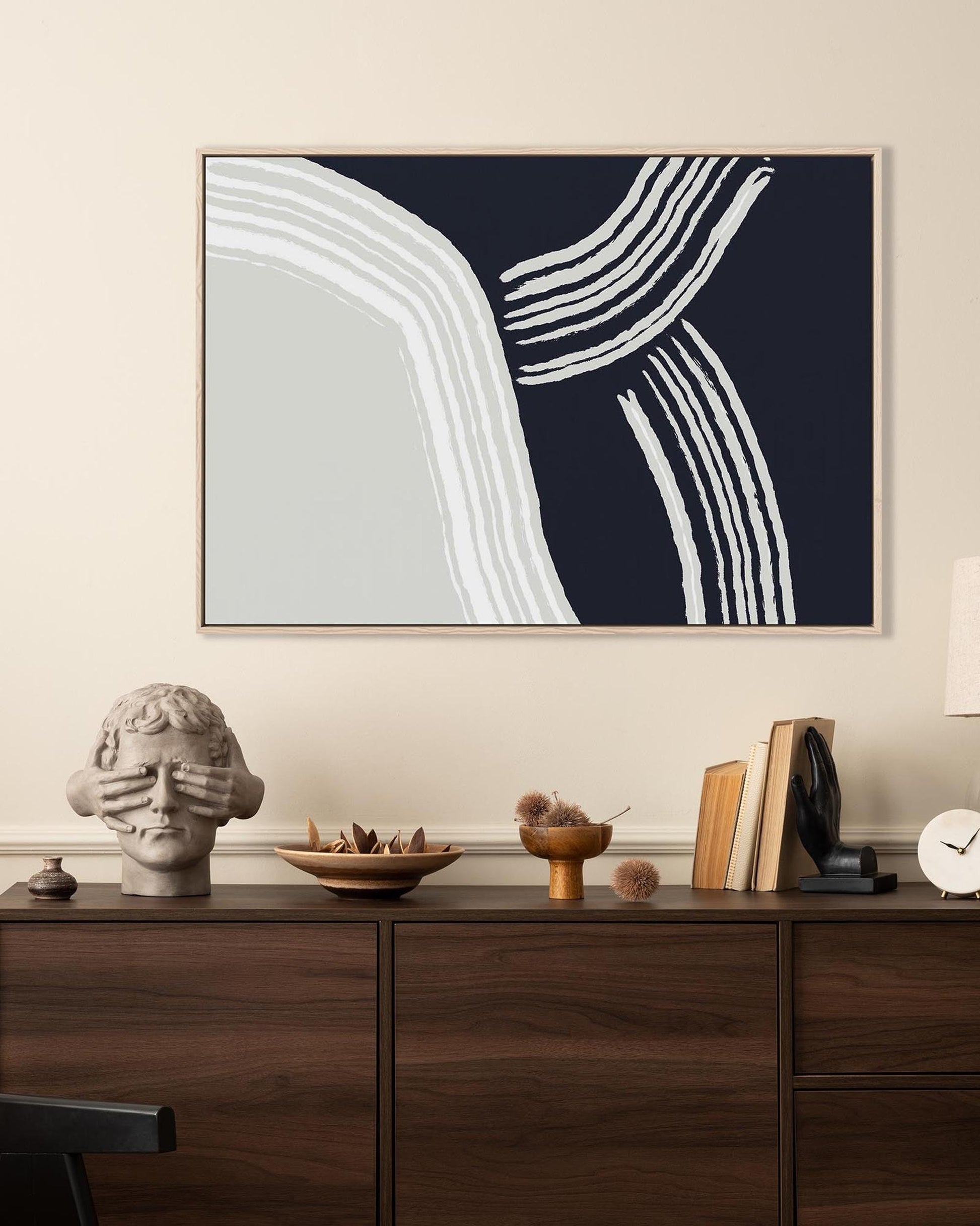 Abstract art piece with white lines on a dark blue background above a wooden cabinet with decorative items.