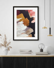 Framed abstract art print on a wall above a shelf with decor items.