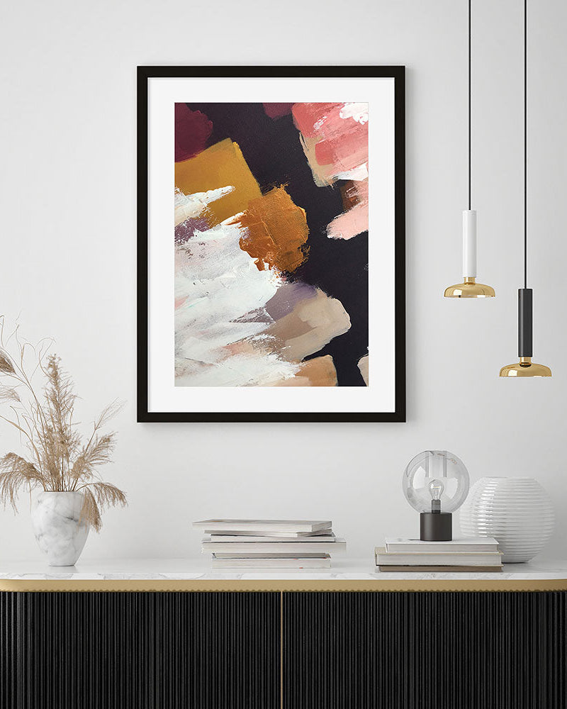 Framed abstract art print on a wall above a shelf with decor items.