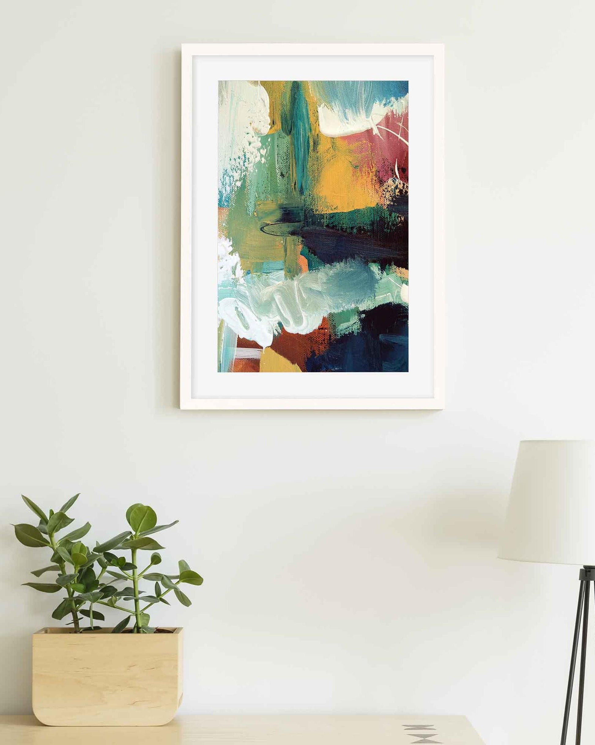 Framed abstract art piece on a wall with a plant and lamp in the foreground.