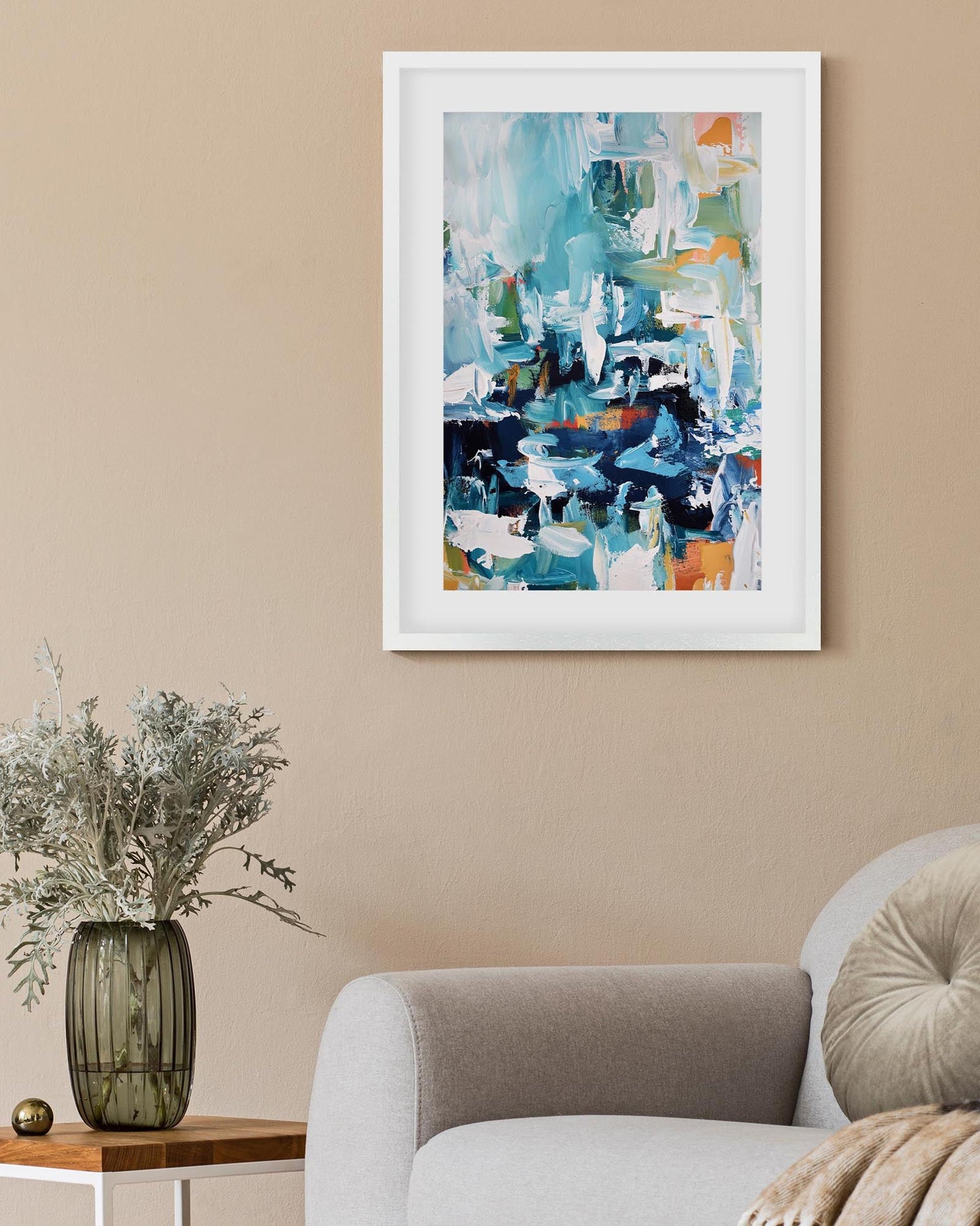 Abstract art print on a beige wall above a vase with flowers on a table.
