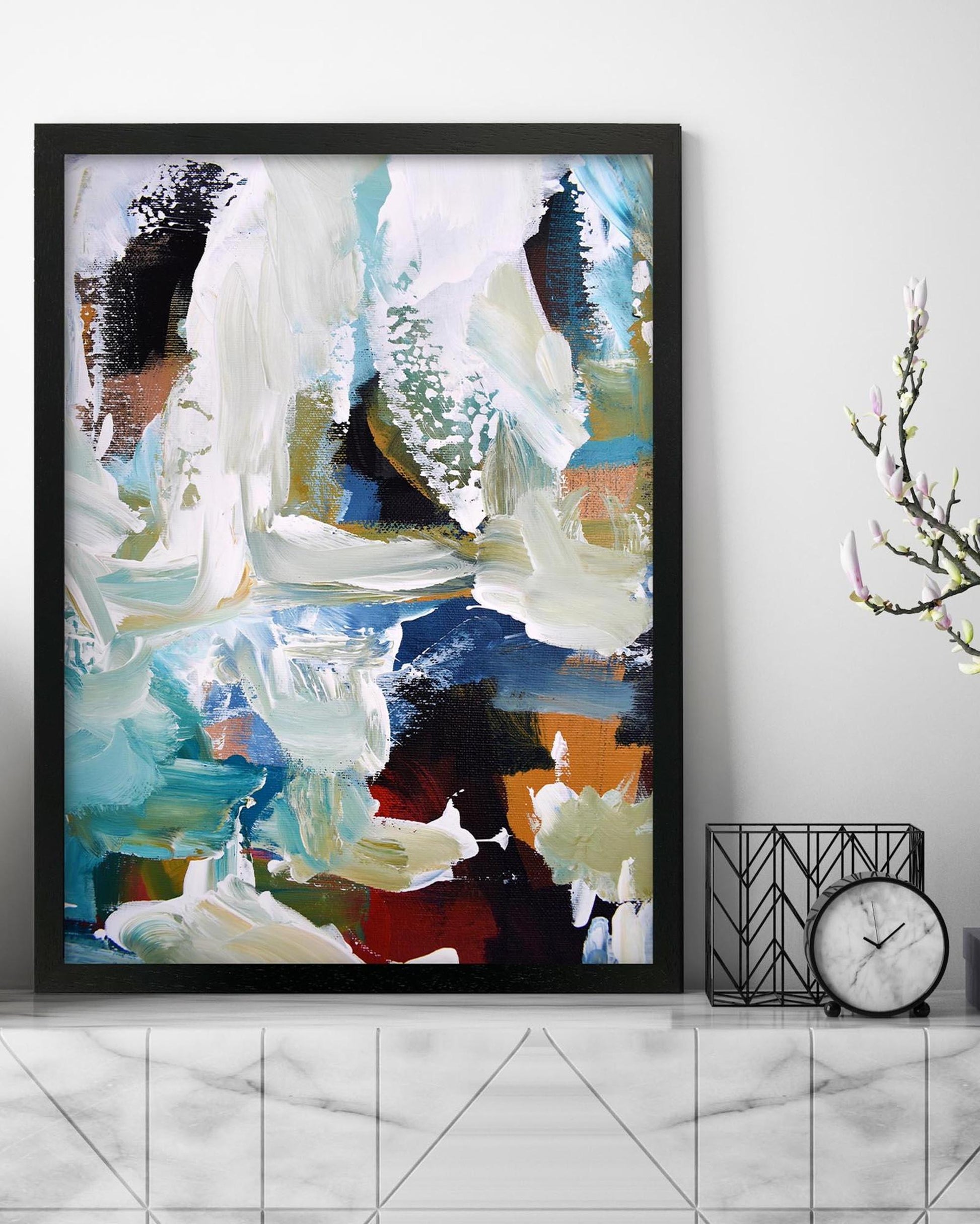Framed abstract art piece on a wall with a clock and decorative item below.