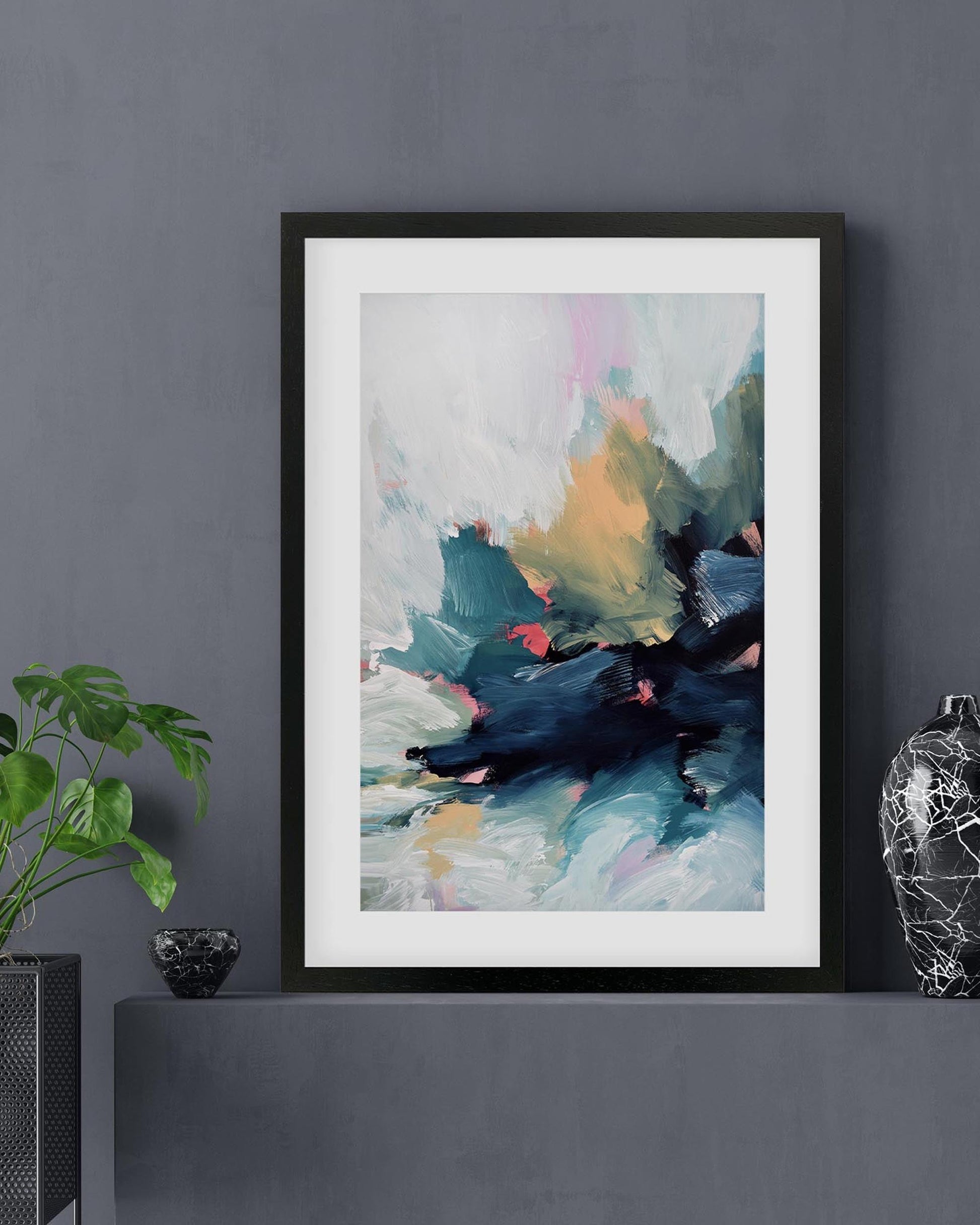 Framed abstract art print on a dark gray wall with decorative items.