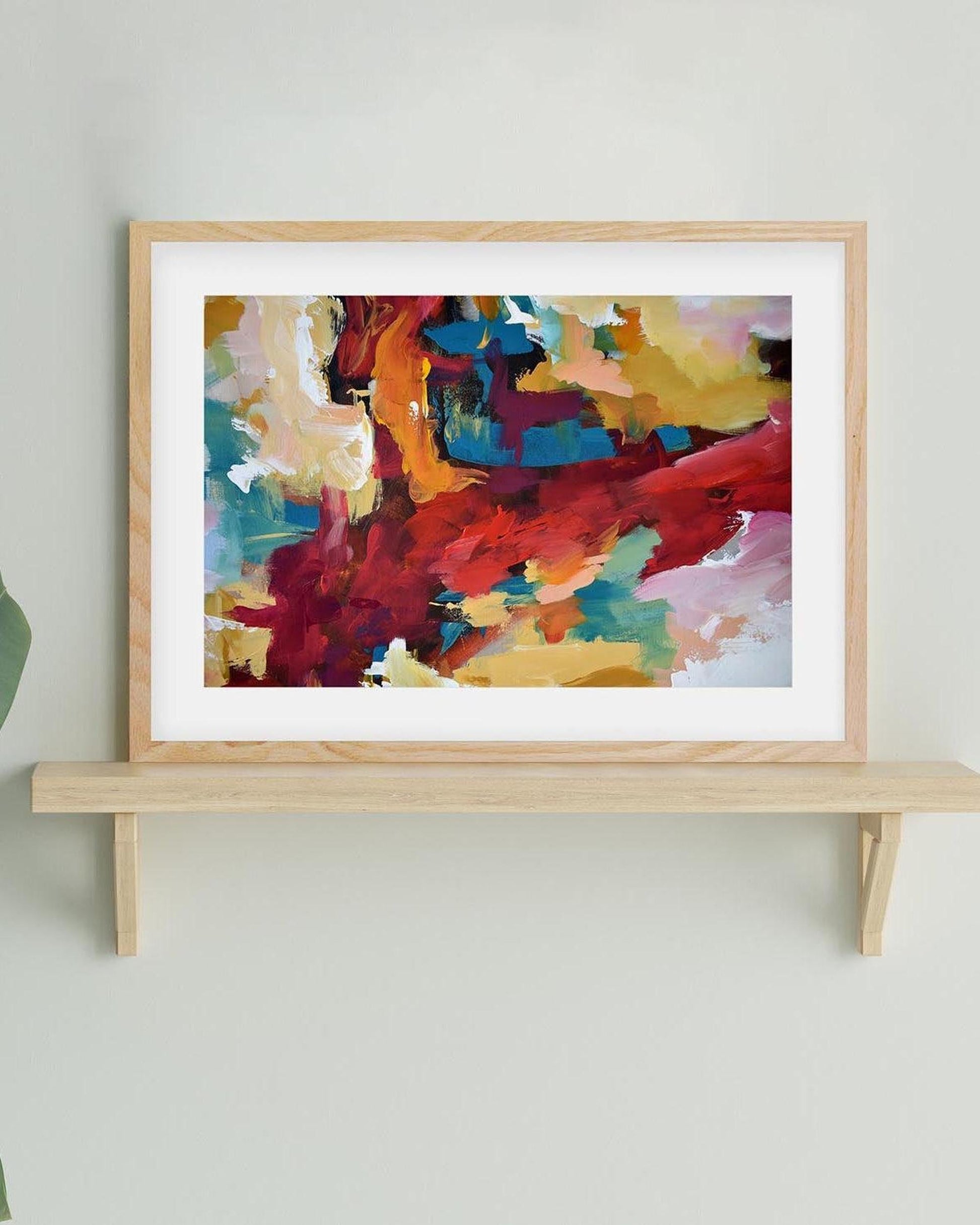 Colorful abstract painting in a wooden frame on a light gray wall.