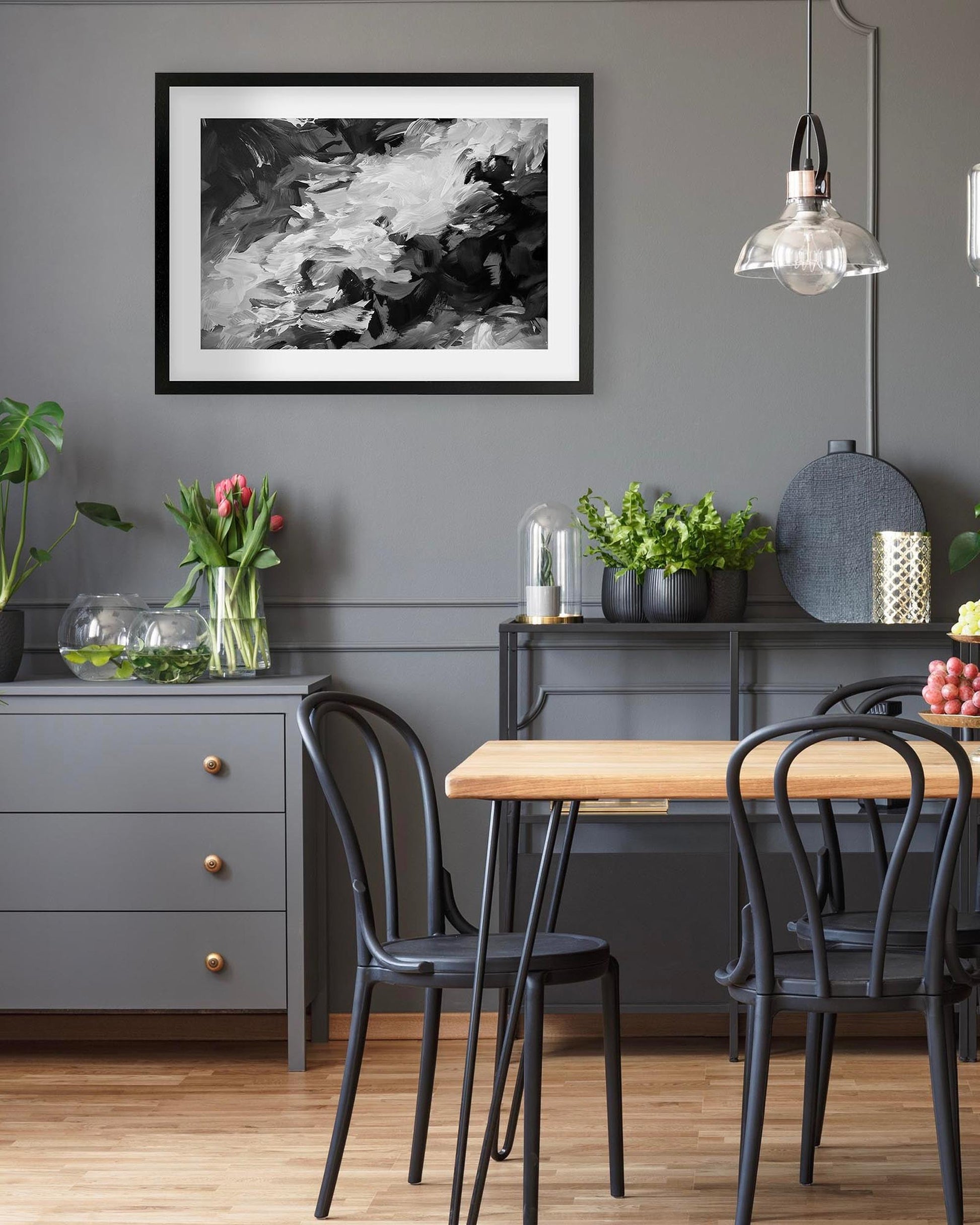 Dining room with a wooden table, black chairs, and a gray wall with framed art.