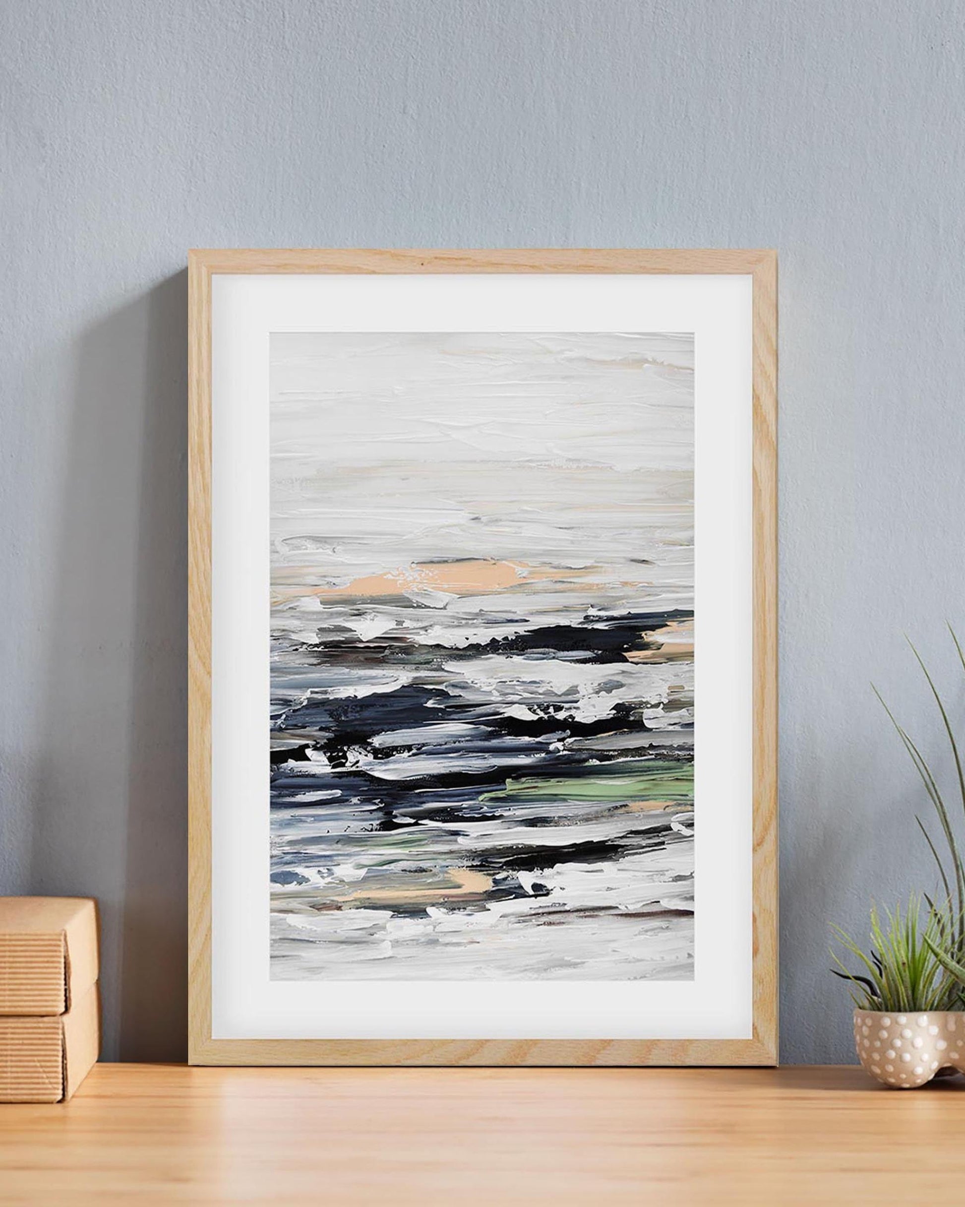 Framed abstract art print on a wall with a plant and wooden boxes below.