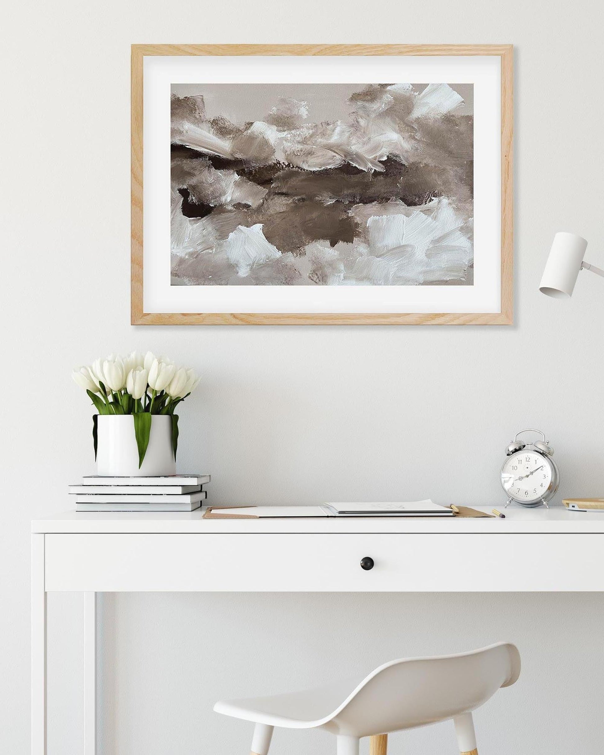Framed abstract art piece on a wall above a desk with decor items.