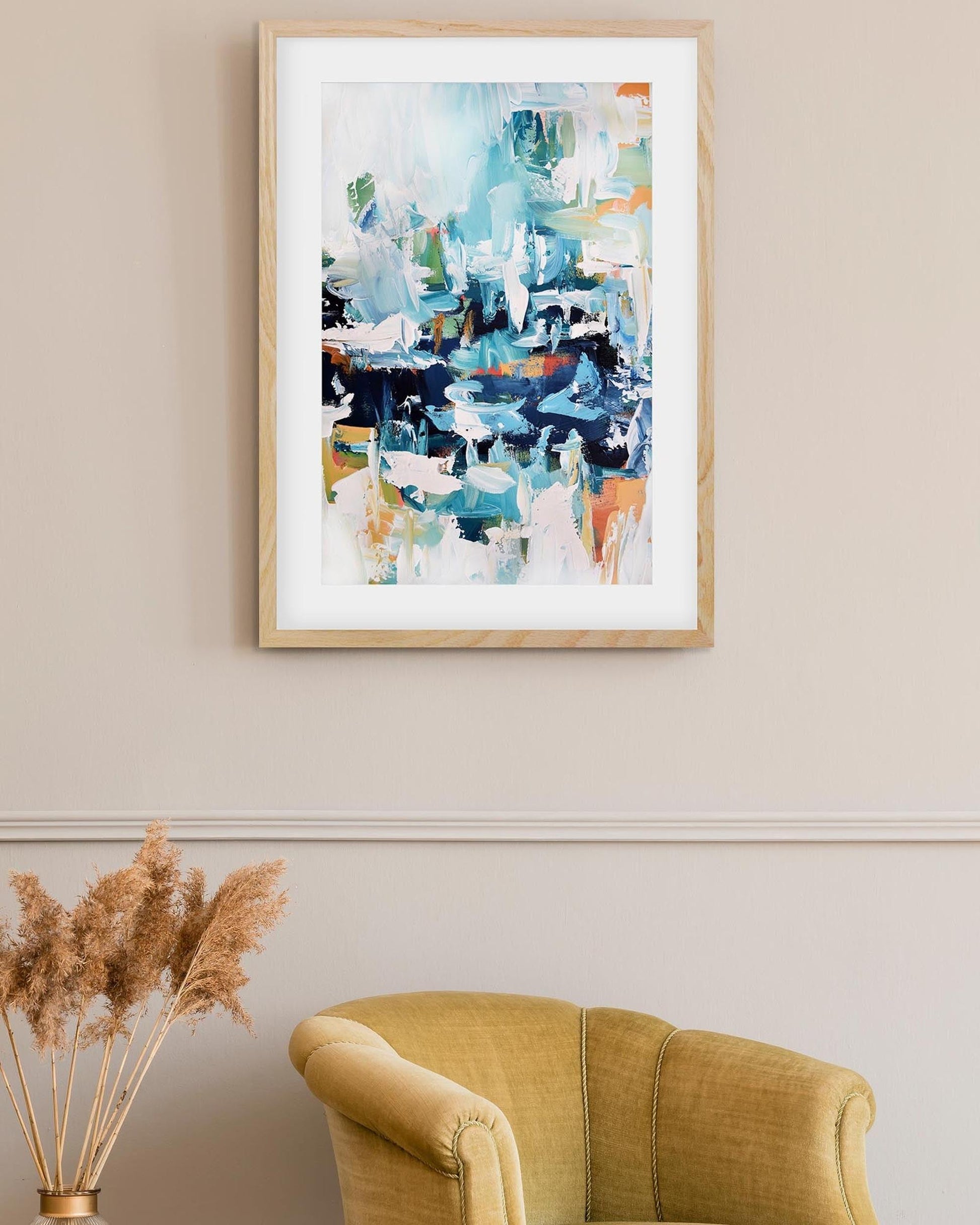 Framed abstract art on a wall above a yellow armchair with decorative elements.