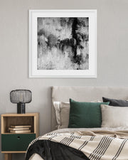 Framed abstract art piece on a wall above a bed with green and beige pillows.