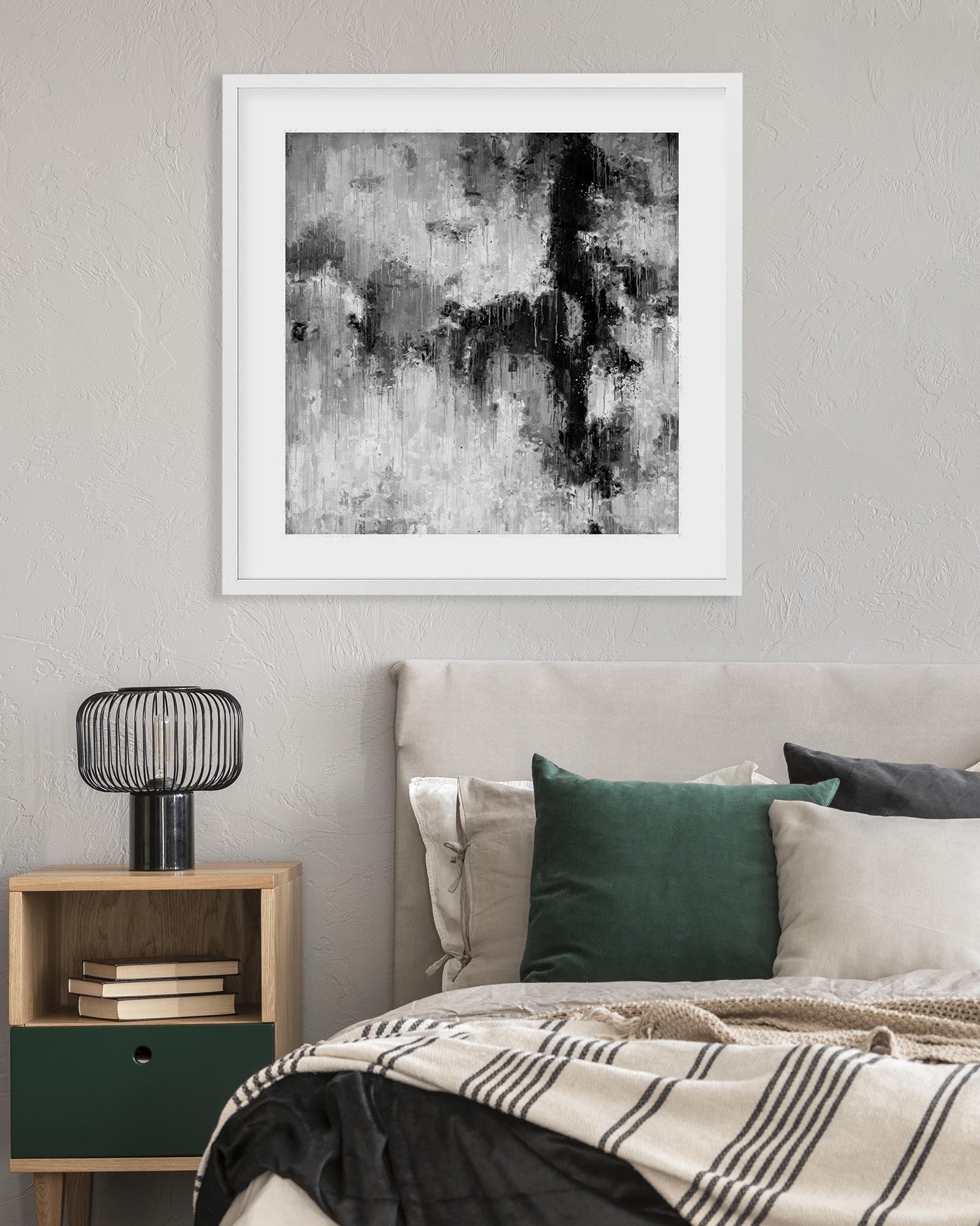 Framed abstract art piece on a wall above a bed with green and beige pillows.