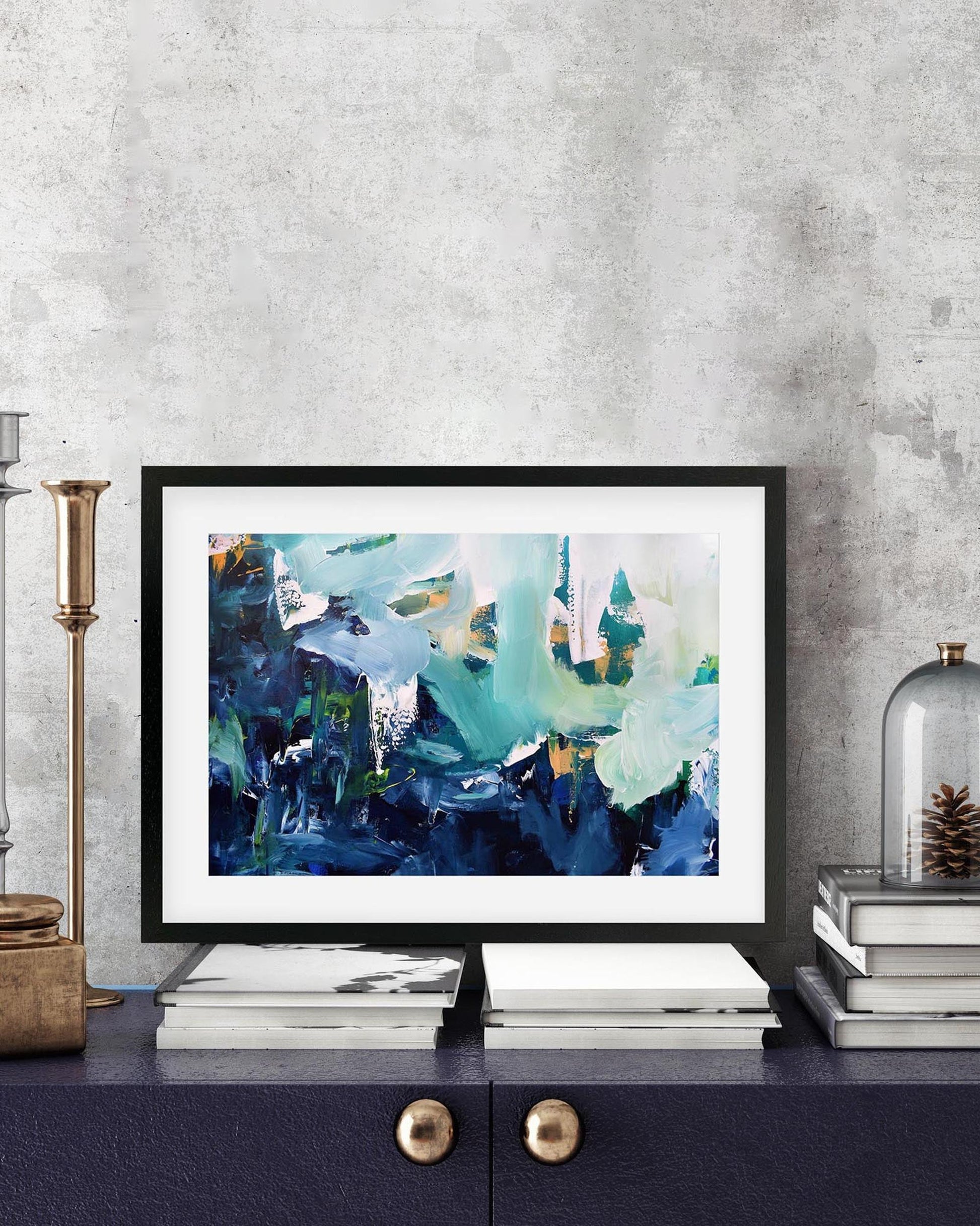 Framed abstract art piece on a shelf with decorative items against a gray wall.