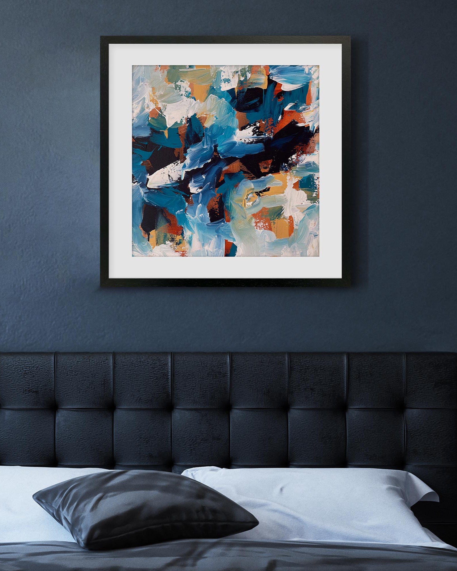 Framed abstract painting on a dark blue wall above a bed with a tufted headboard.