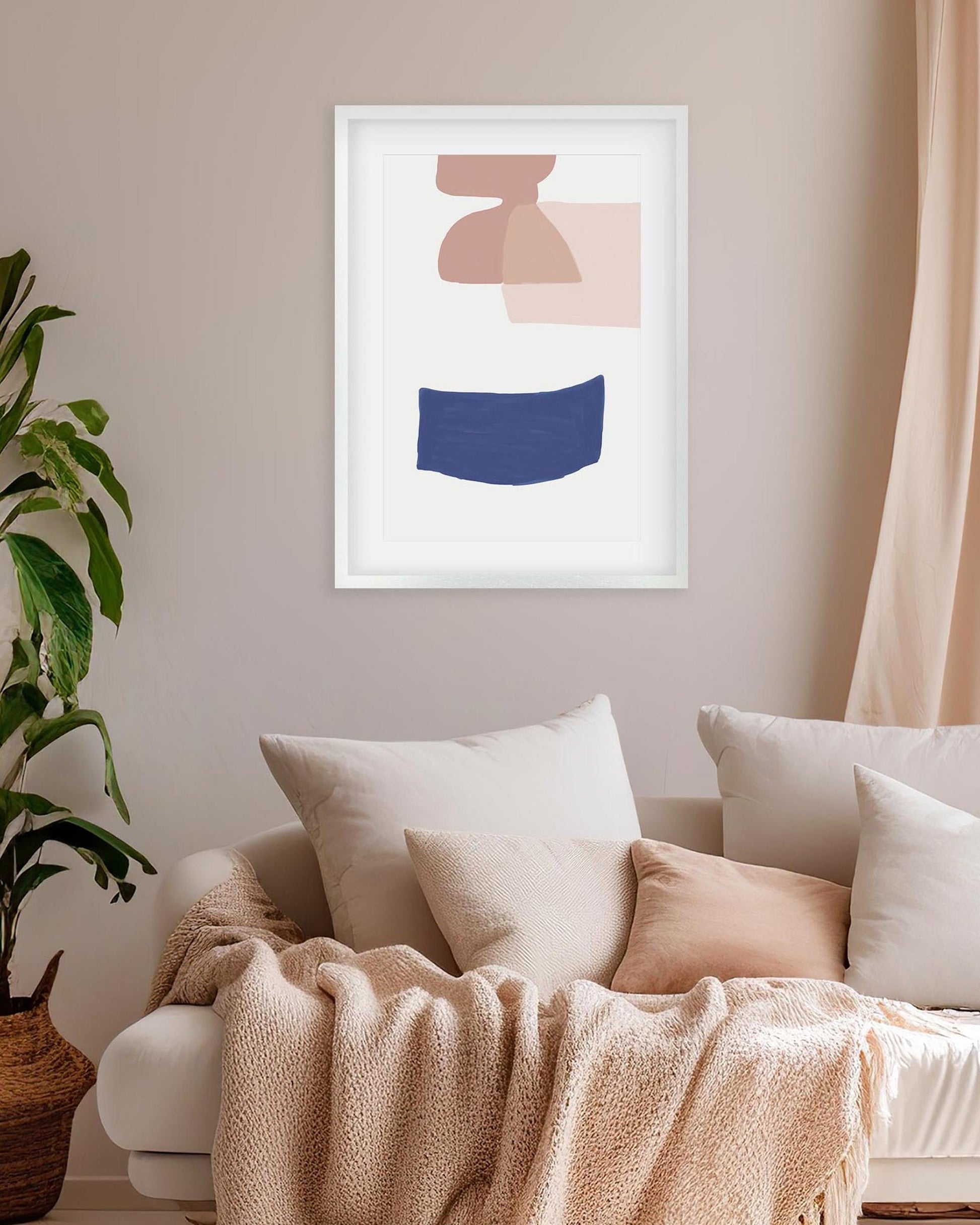 Abstract art print on a wall above a sofa with pillows and a blanket.