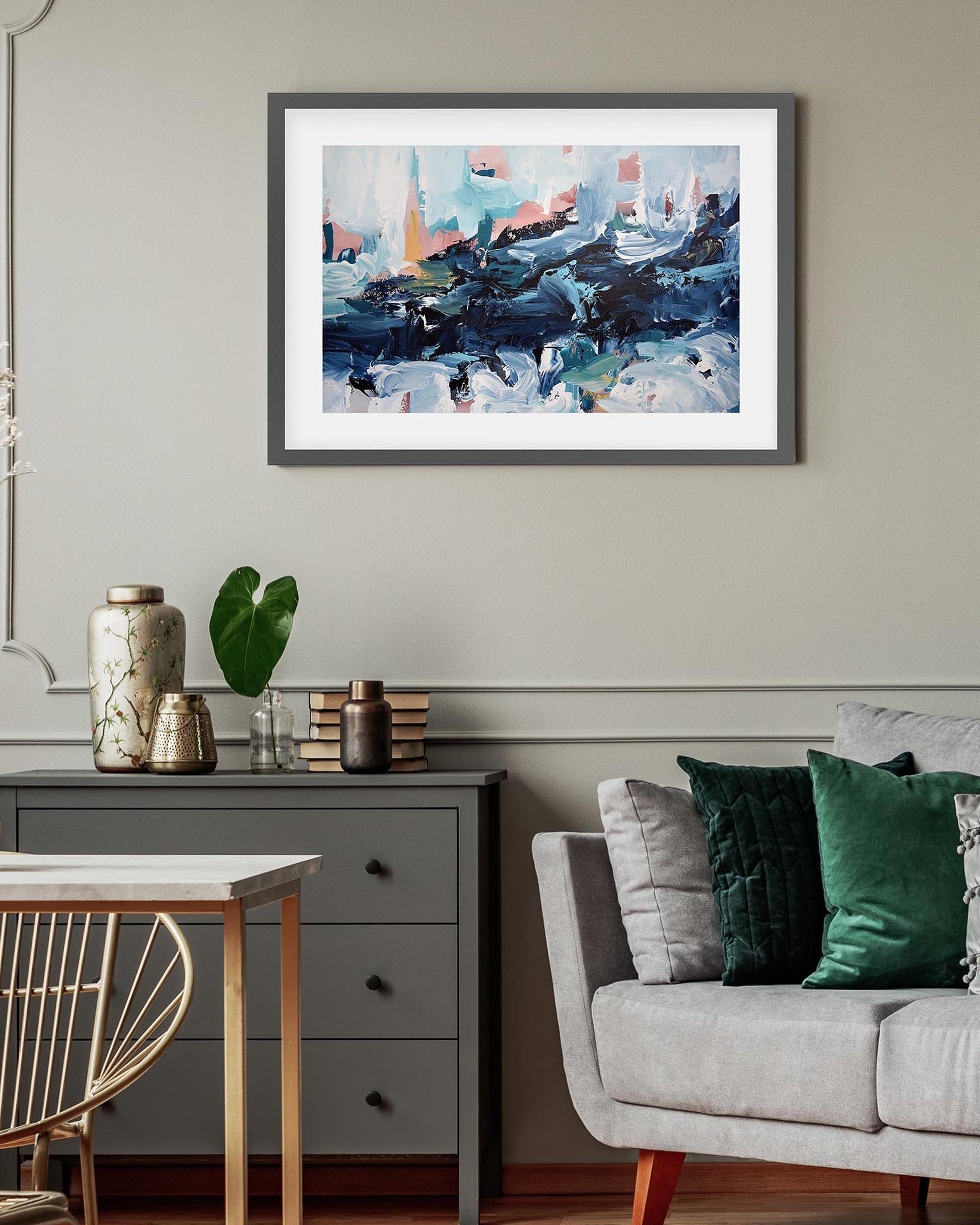 Living room with a gray sofa, decorative pillows, a small table with vases, and a framed abstract painting on the wall.