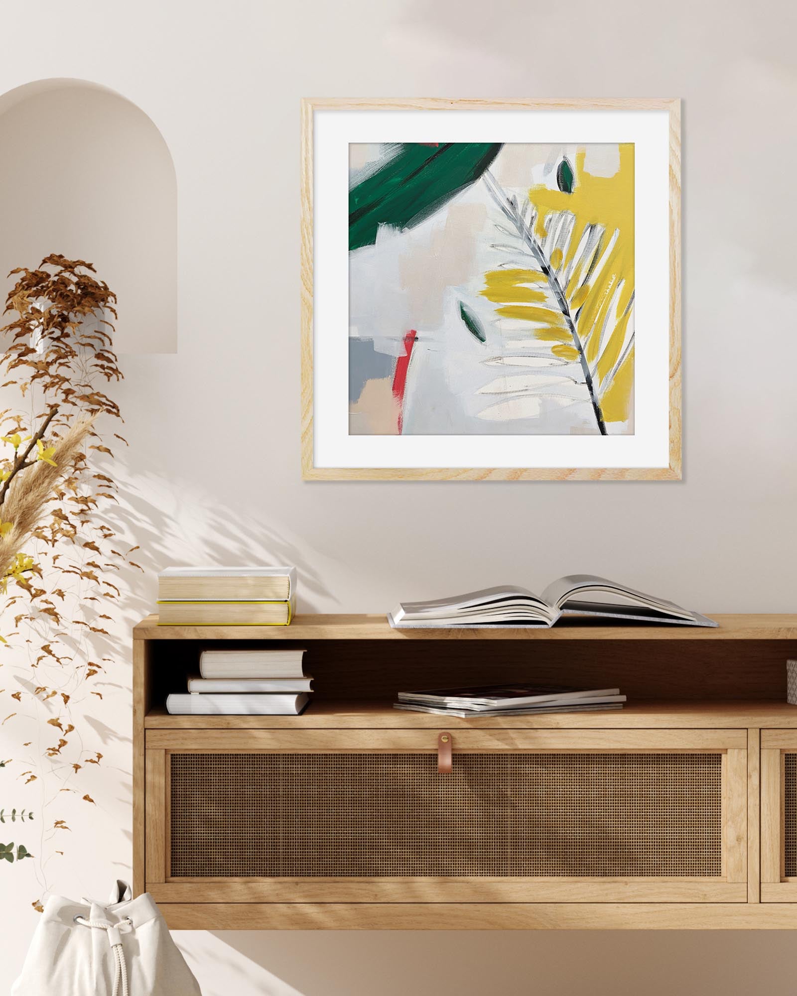 Framed abstract art piece on a wall above a wooden cabinet with books.