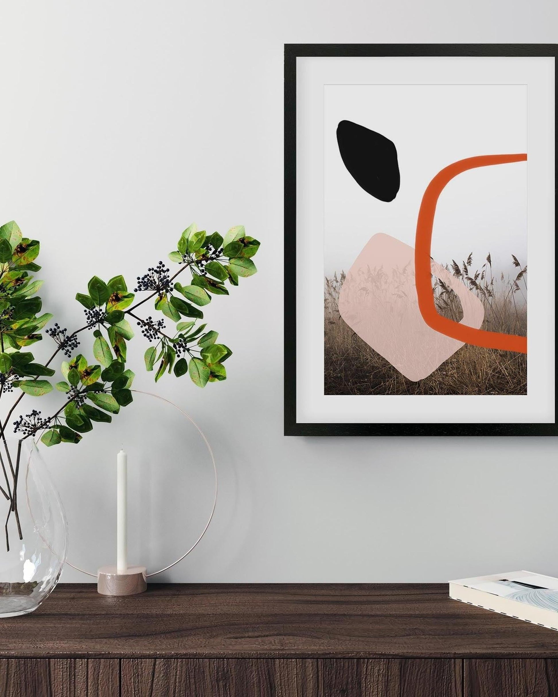 Abstract art print on a wall above a wooden surface with a vase and candle.