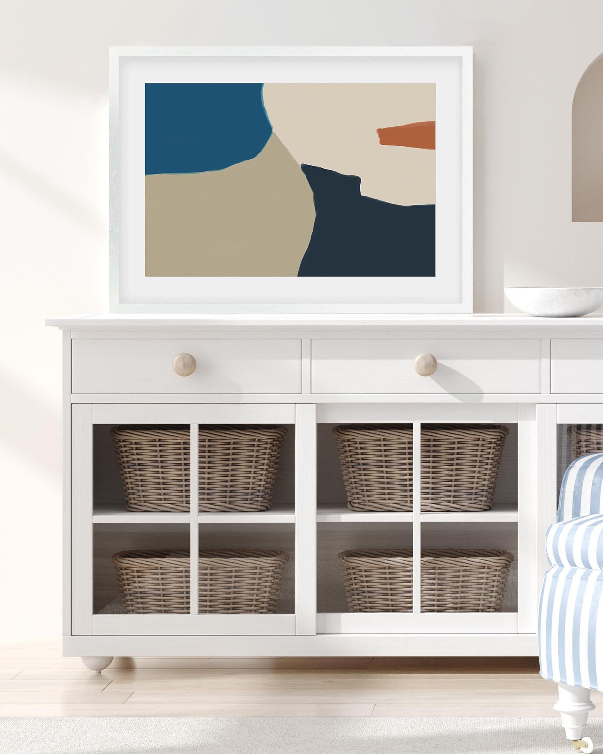 Framed abstract art above a white cabinet with wicker baskets.