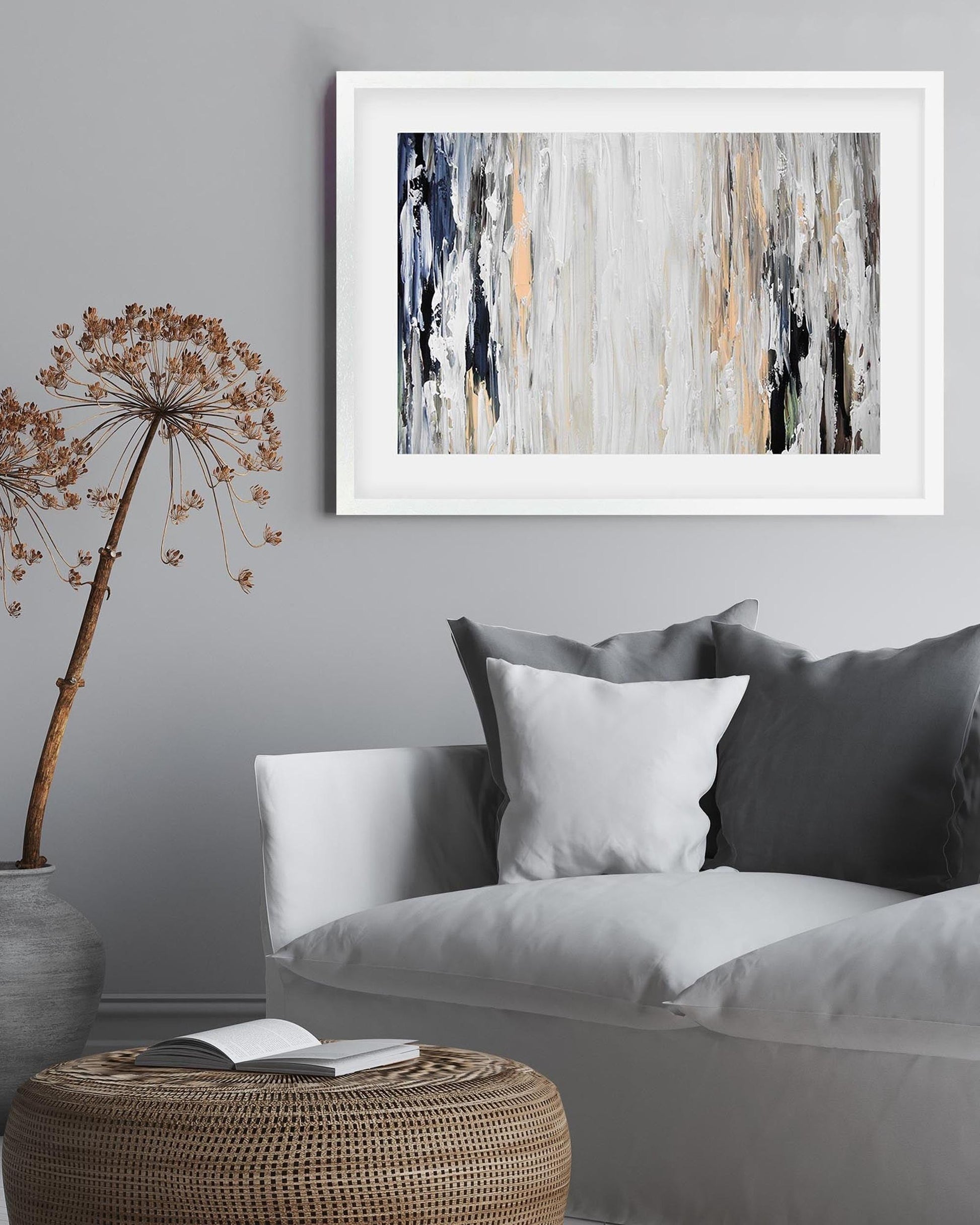 Living room with a gray sofa, decorative pillows, a woven ottoman, and abstract art on the wall.