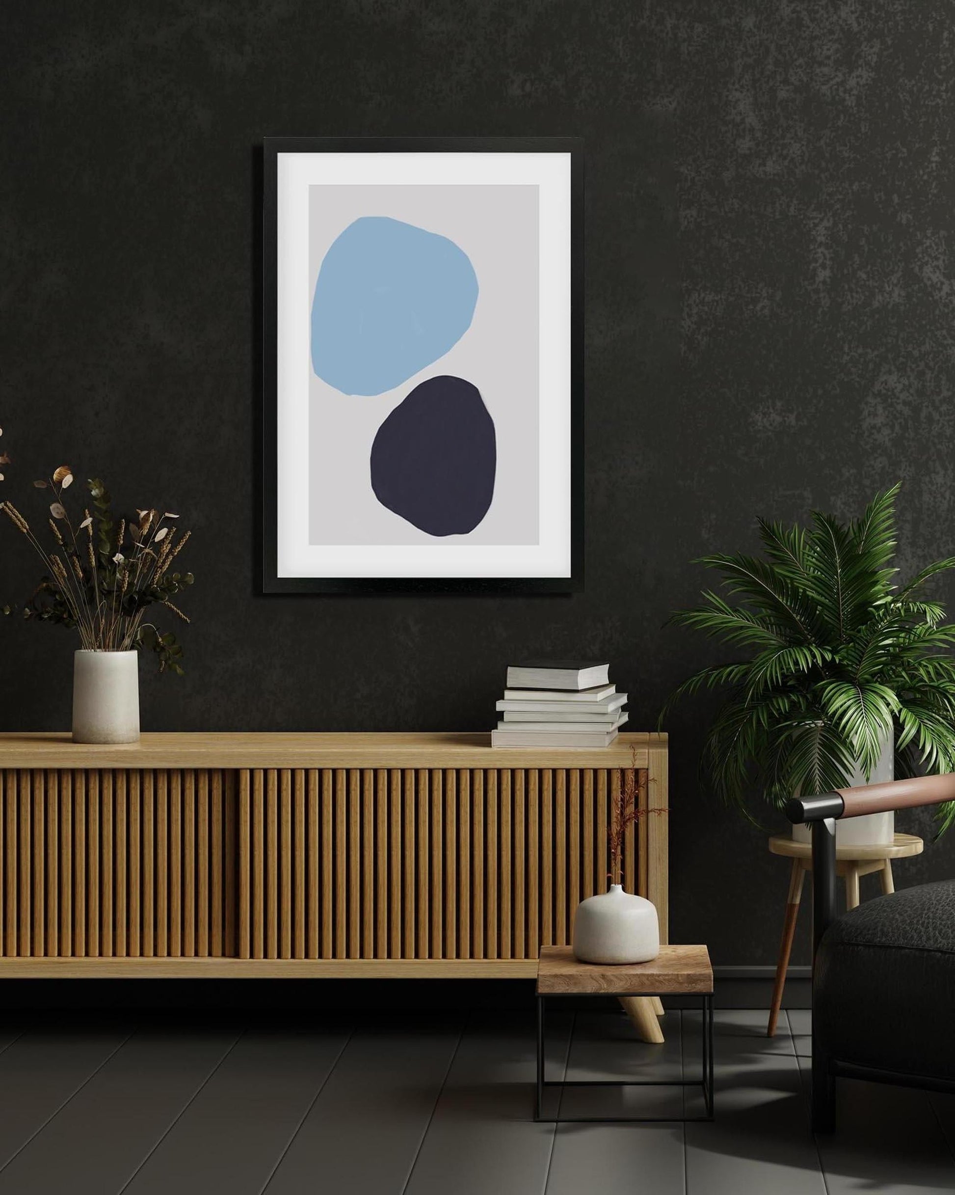 Abstract art print with blue and black shapes on a dark wall above a wooden cabinet.