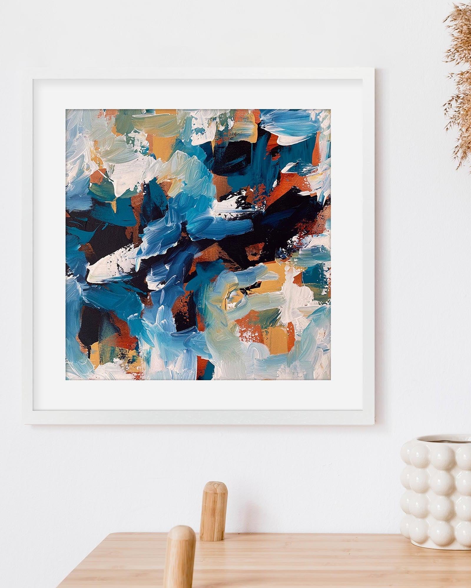 Framed abstract painting with blue, orange, and white colors on a white wall.
