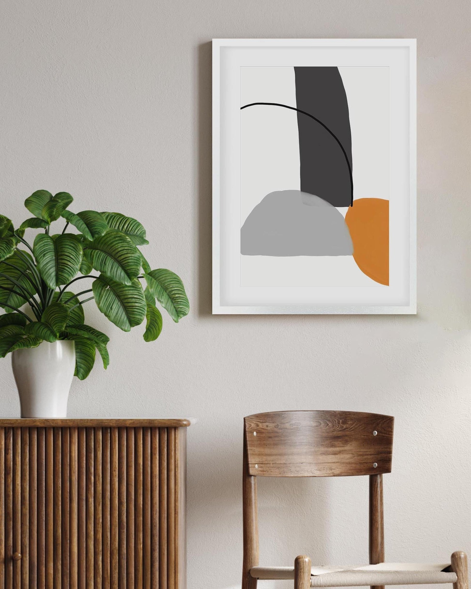 Abstract art print on a wall with a plant and wooden chair below.
