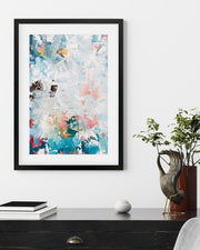Framed abstract art piece on a wall above a desk with decorative items.