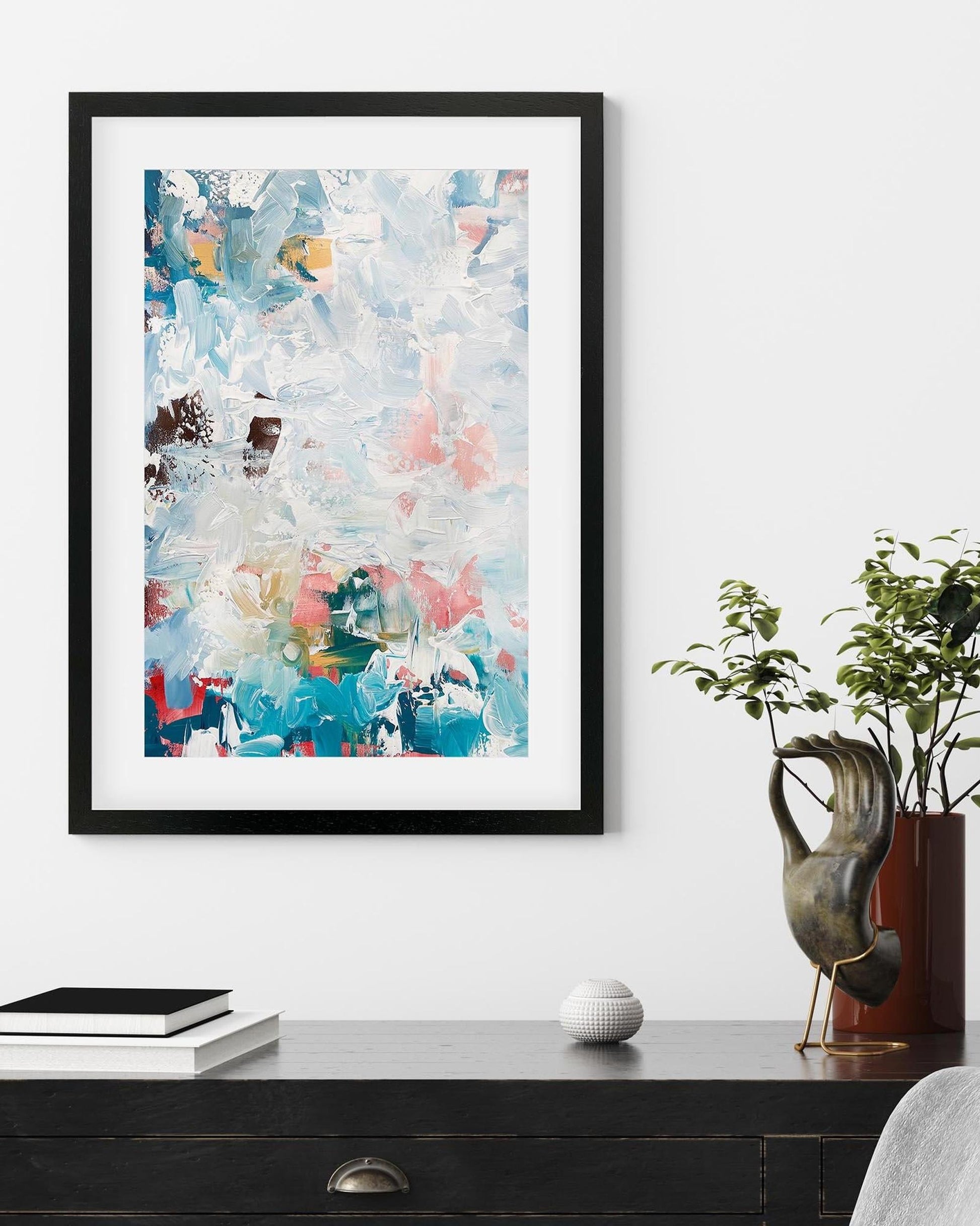 Framed abstract art piece on a wall above a desk with decorative items.