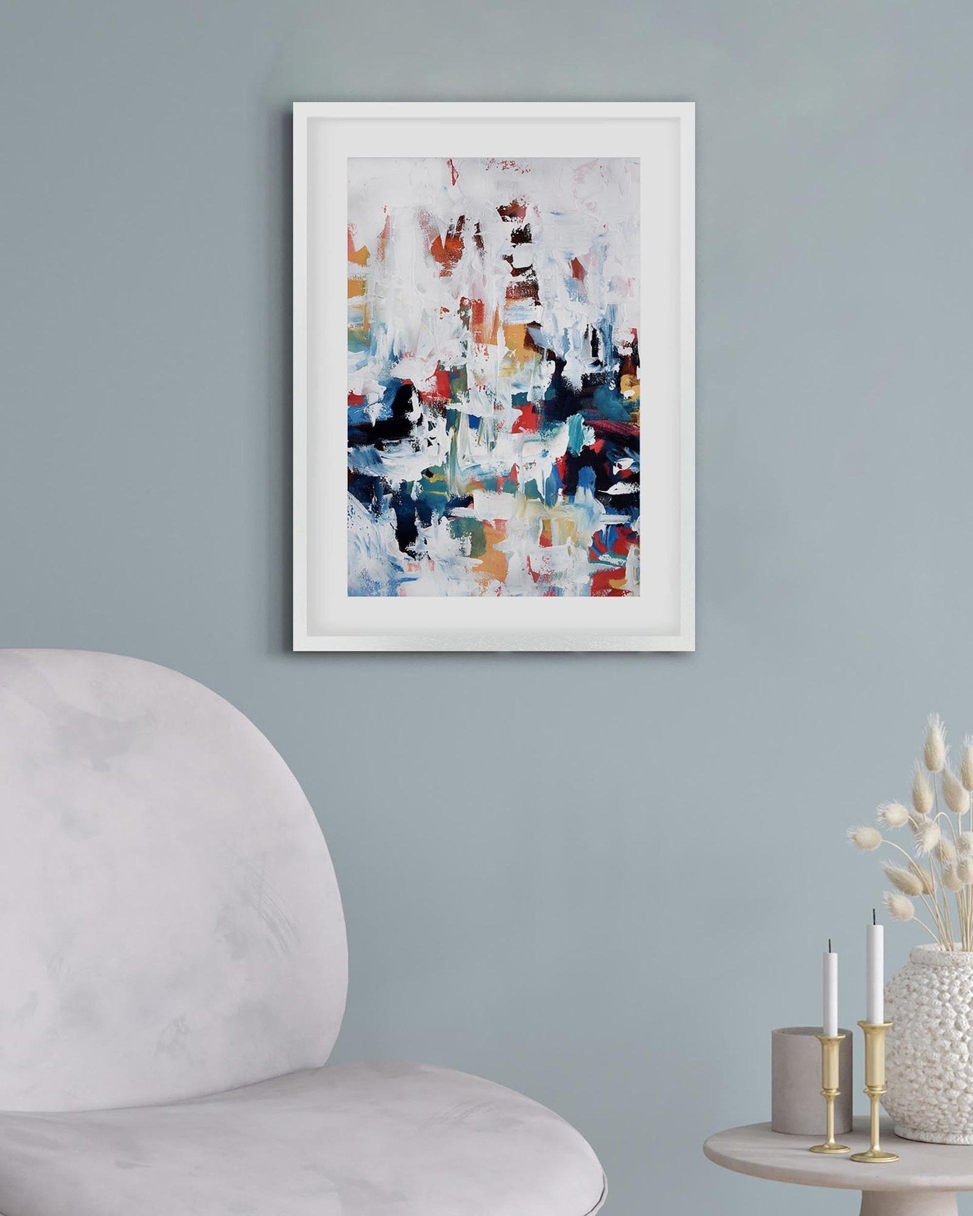 Framed abstract art piece on a gray wall with a chair and table in the foreground.