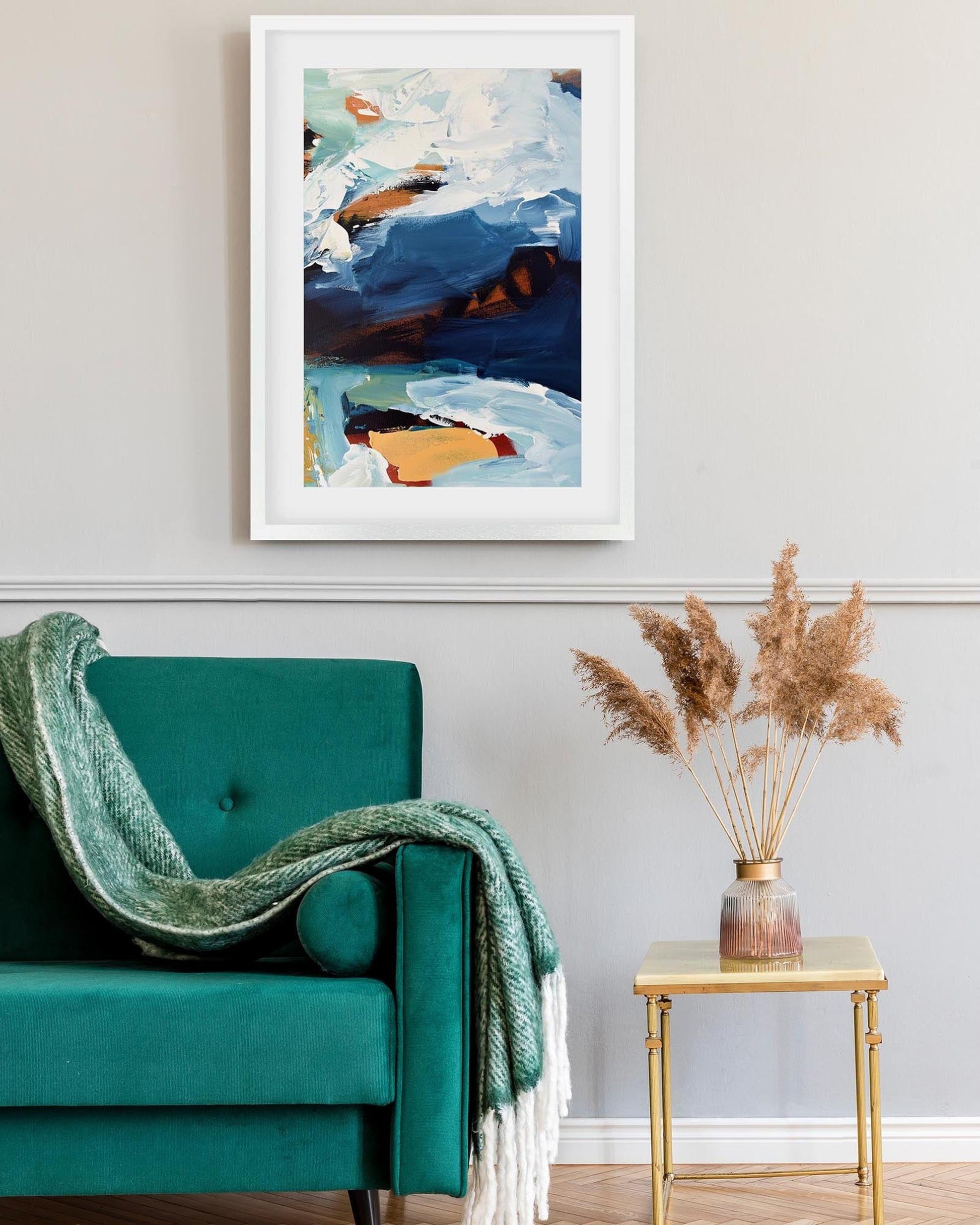 Teal armchair with a green blanket, abstract painting on the wall, and a small table with dried plants.