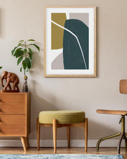 Abstract art print in a wooden frame on a wall above a wooden cabinet and stool.