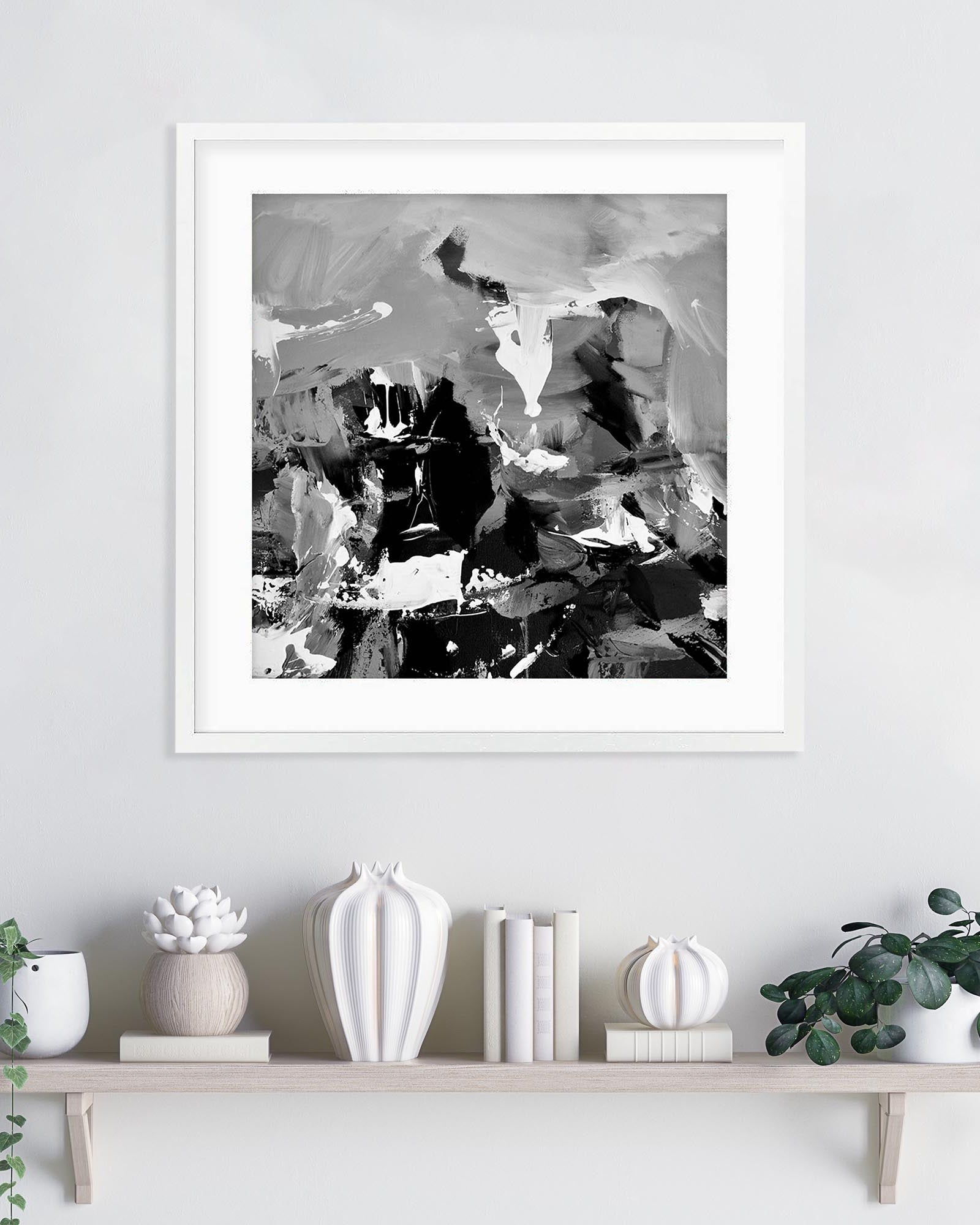 Framed abstract black and white artwork on a wall above a shelf with decorative items.