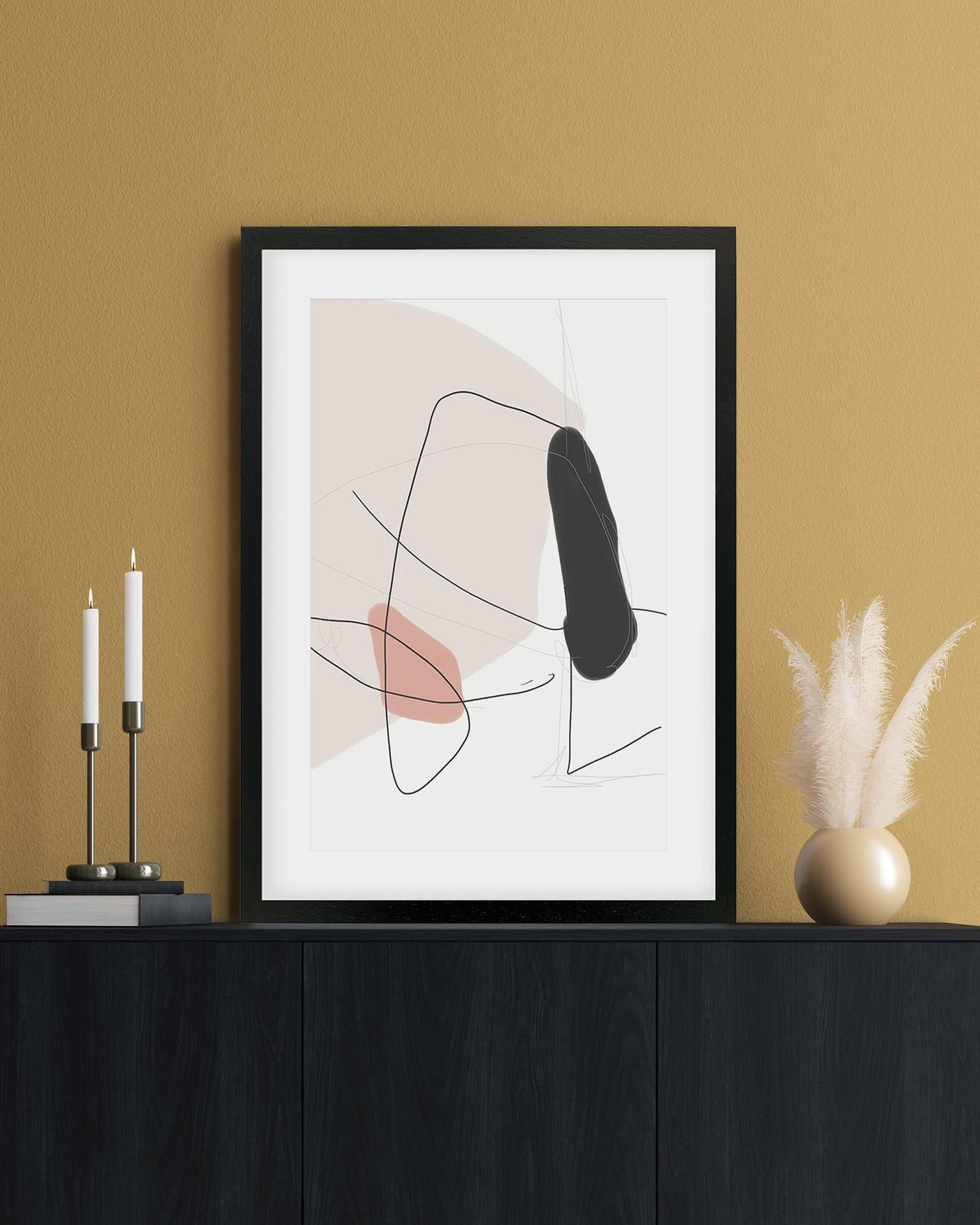 Abstract art print in a black frame on a mustard yellow wall with decorative items.