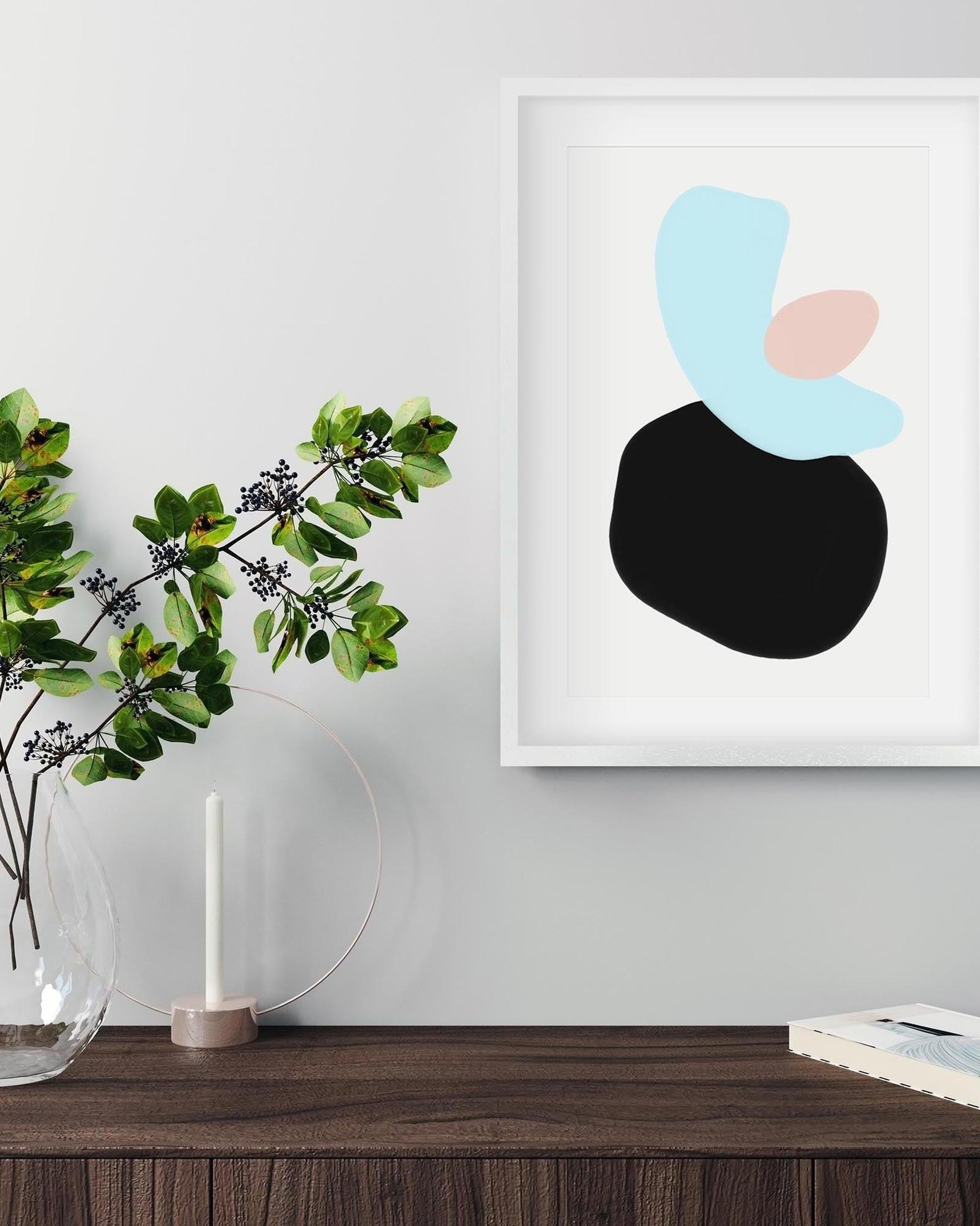 Framed abstract art piece on a wall above a wooden surface with a plant and candle.