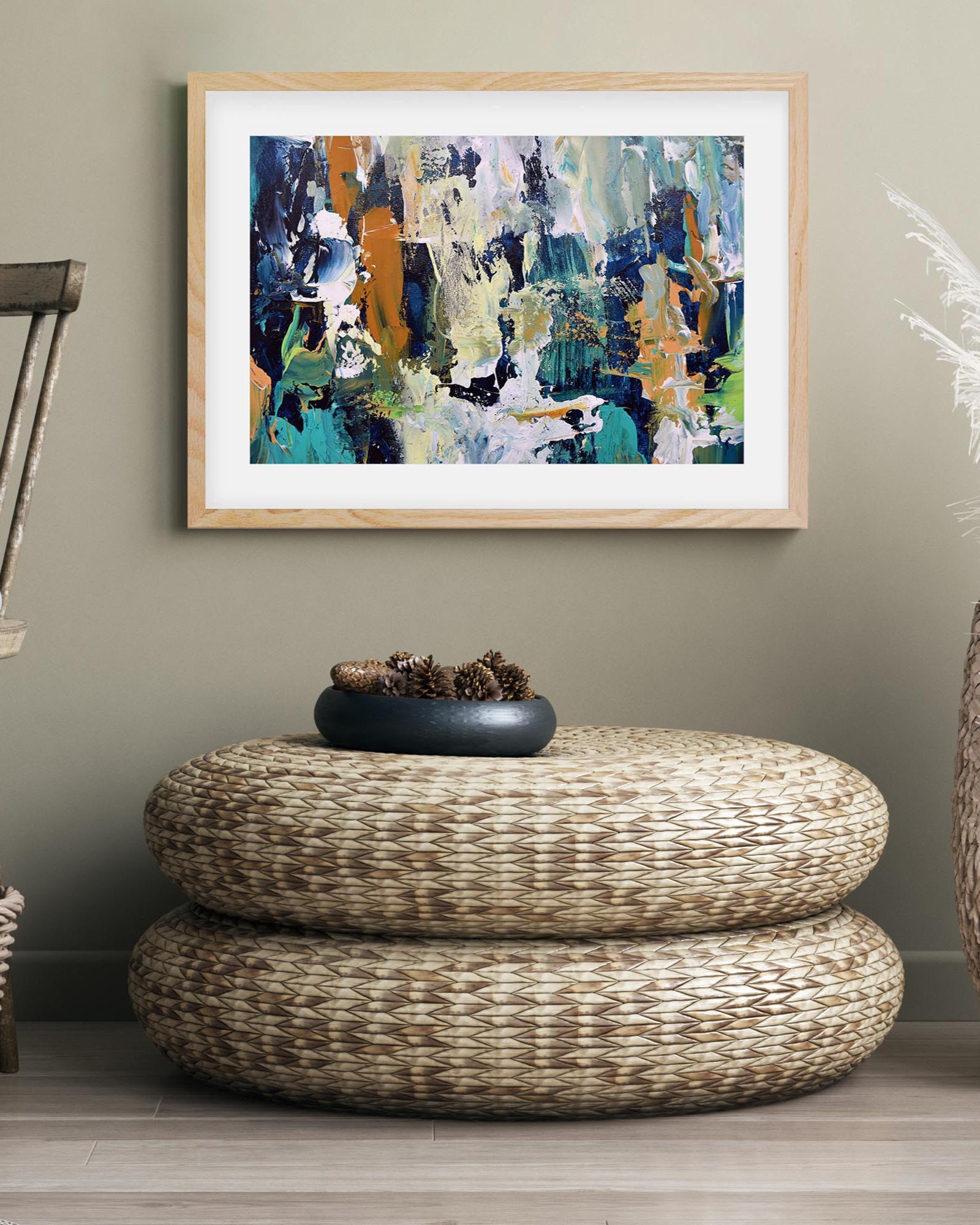Abstract painting on a wall above a woven ottoman with a decorative bowl.