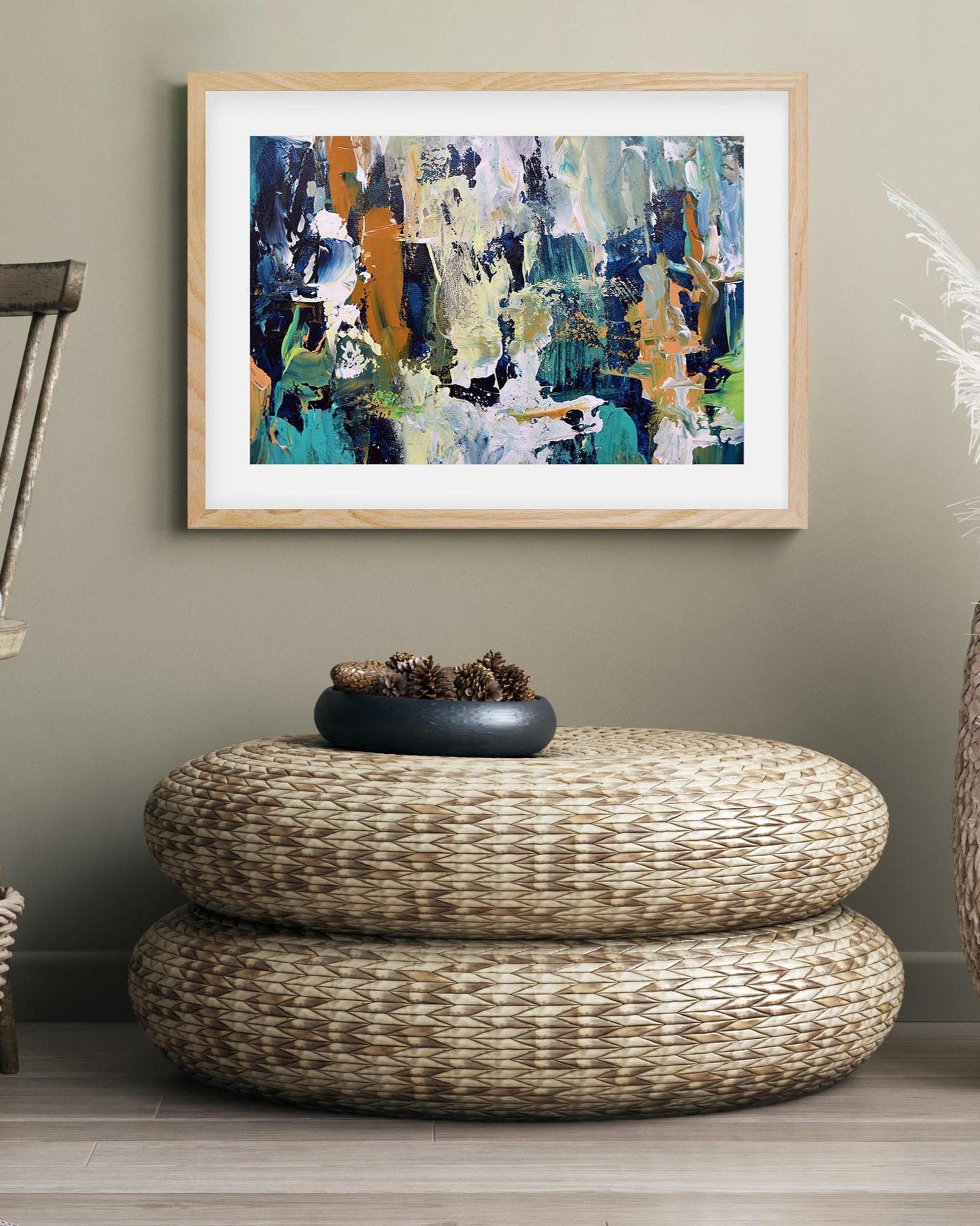 Abstract painting on a wall above a woven ottoman with a decorative bowl.