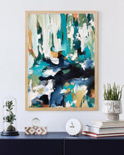 Abstract painting in a wooden frame on a wall with decorative items below.