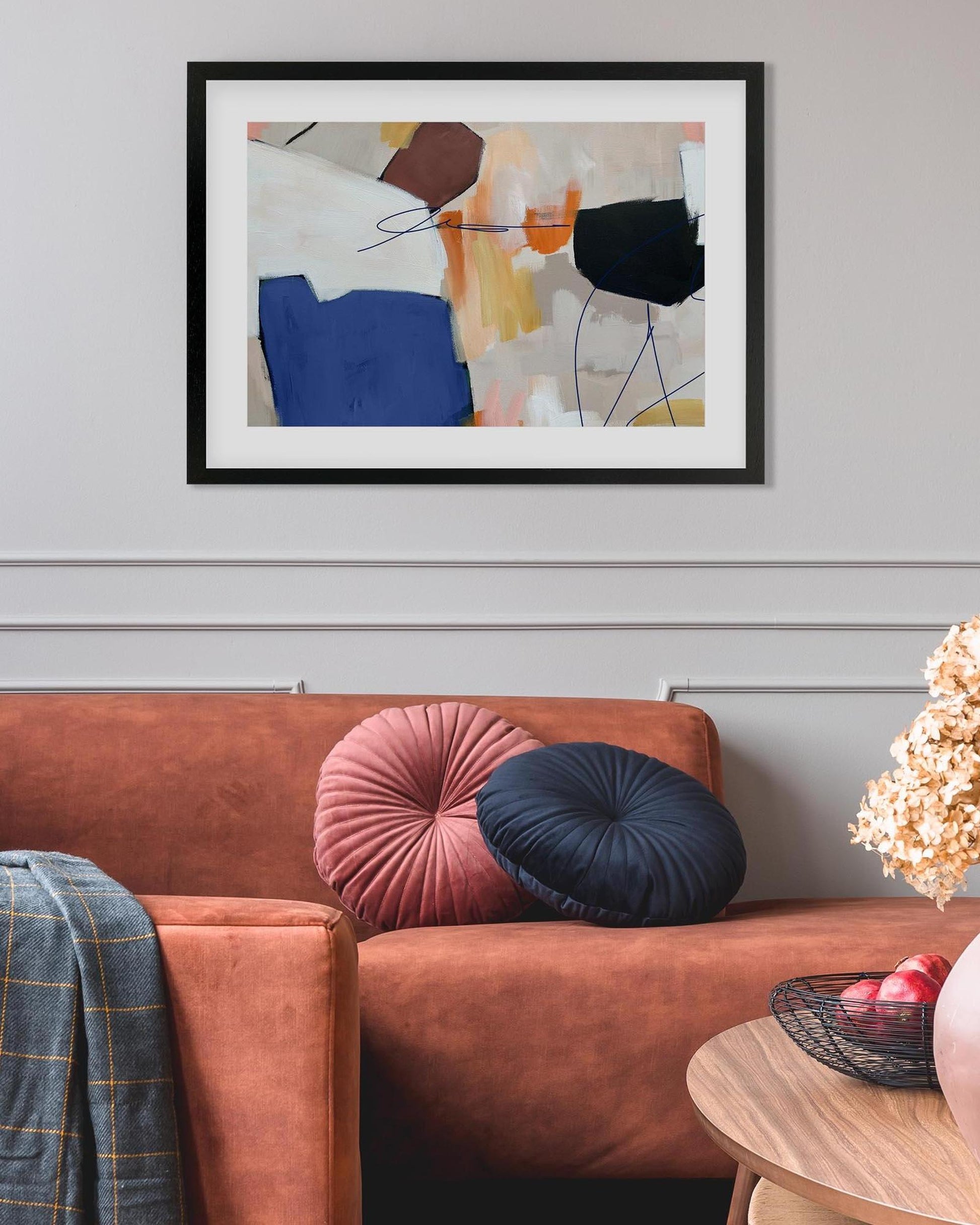 Framed abstract art above a brown sofa with decorative pillows and a small table.