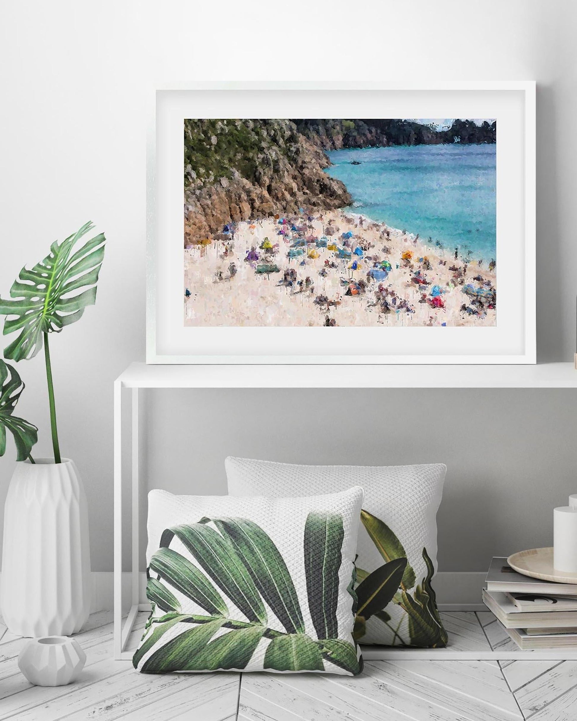 Framed photograph of a beach scene on a wall above decorative pillows with leaf patterns.
