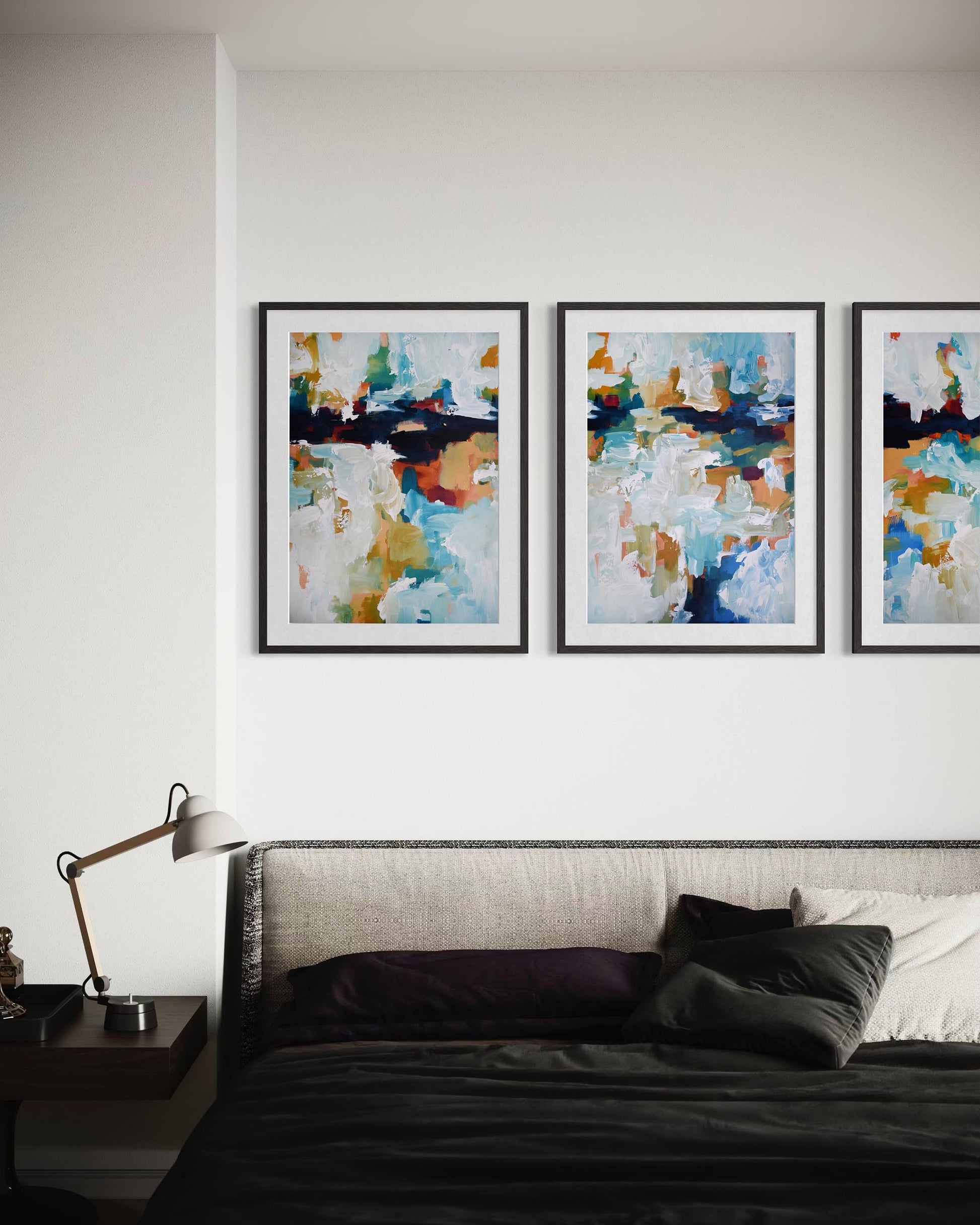 Three abstract paintings on a wall above a bed in a bedroom setting.