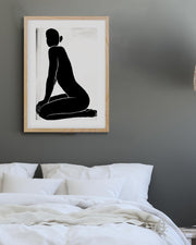 Framed black and white artwork of a seated figure on a gray wall above a bed.