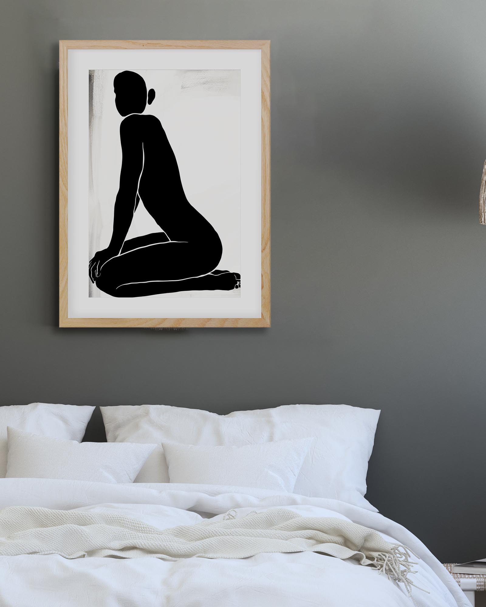 Framed black and white artwork of a seated figure on a gray wall above a bed.