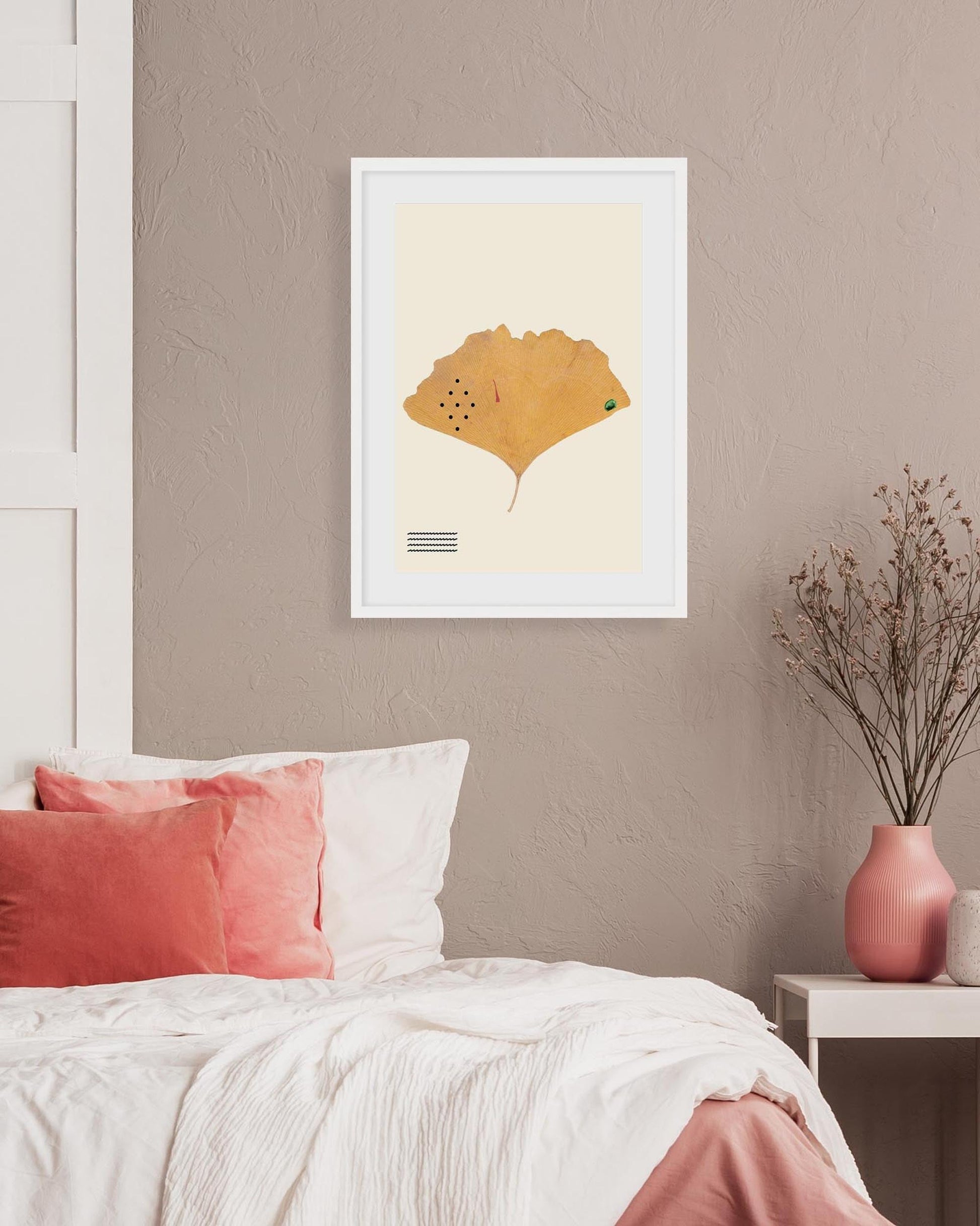 Framed artwork of a yellow leaf on a beige wall above a bed with pink and white pillows.