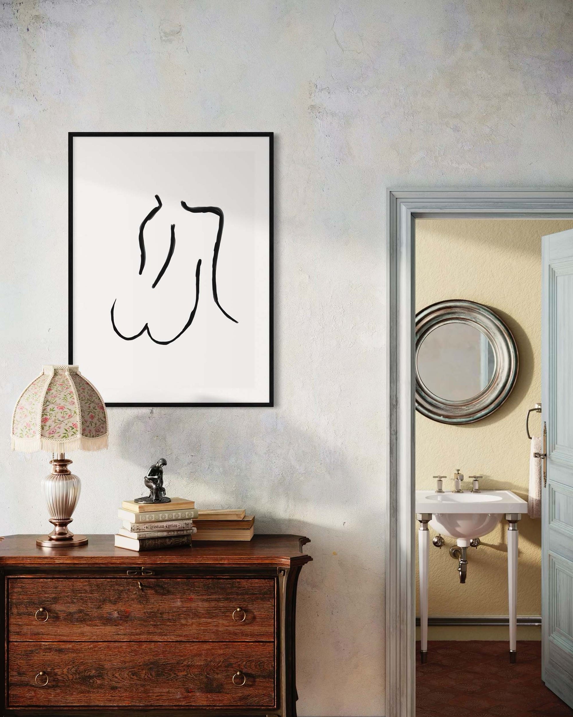 Framed black and white artwork on a wall next to a wooden dresser with a lamp and books.