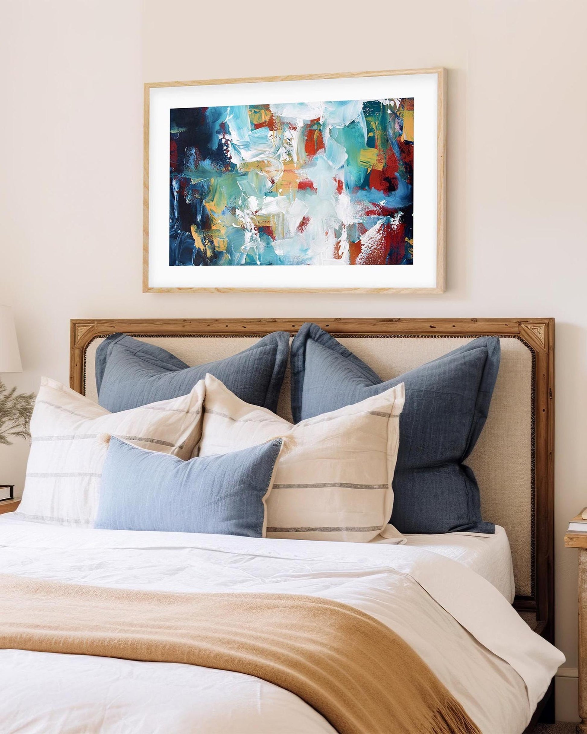 Bedroom with a bed featuring blue and beige pillows, a wooden headboard, and a colorful abstract painting above.